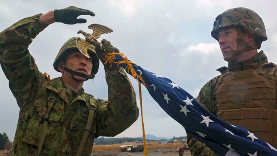 Japan Ground Self-Defense Force Sgt. 1st Class Yatsuka Ikeda, left, helps U.S. Marine 1st Sgt. Timothy Babcock set up the American flag Dec. 1 before the opening ceremony for Forest Light 15-1 at the Oyanohara Training Area in Yamato, Kumamoto prefecture, Japan. Forest Light demonstrates the continued commitment of the U.S. and Japan to increase interoperability of our armed forces and maintain a strong partnership to protect Japan from external aggression. Ikeda is with 42nd Regiment, 8th Division, Western Army, JGSDF. Babcock, from Port Austin, Michigan, is company first sergeant with Company G, 2nd Battalion, 9th Marine Regiment, currently attached to 4th Marine Regiment, 3rd Marine Division, III Marine Expeditionary Force, under the unit deployment program. (U.S. Marine Corps photo by Cpl. Drew Tech/Released)