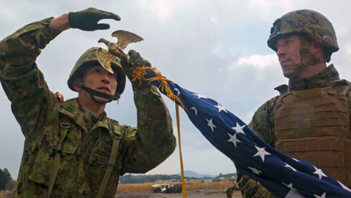 Japan Ground Self-Defense Force Sgt. 1st Class Yatsuka Ikeda, left, helps U.S. Marine 1st Sgt. Timothy Babcock set up the American flag Dec. 1 before the opening ceremony for Forest Light 15-1 at the Oyanohara Training Area in Yamato, Kumamoto prefecture, Japan. Forest Light demonstrates the continued commitment of the U.S. and Japan to increase interoperability of our armed forces and maintain a strong partnership to protect Japan from external aggression. Ikeda is with 42nd Regiment, 8th Division, Western Army, JGSDF. Babcock, from Port Austin, Michigan, is company first sergeant with Company G, 2nd Battalion, 9th Marine Regiment, currently attached to 4th Marine Regiment, 3rd Marine Division, III Marine Expeditionary Force, under the unit deployment program. (U.S. Marine Corps photo by Cpl. Drew Tech/Released)