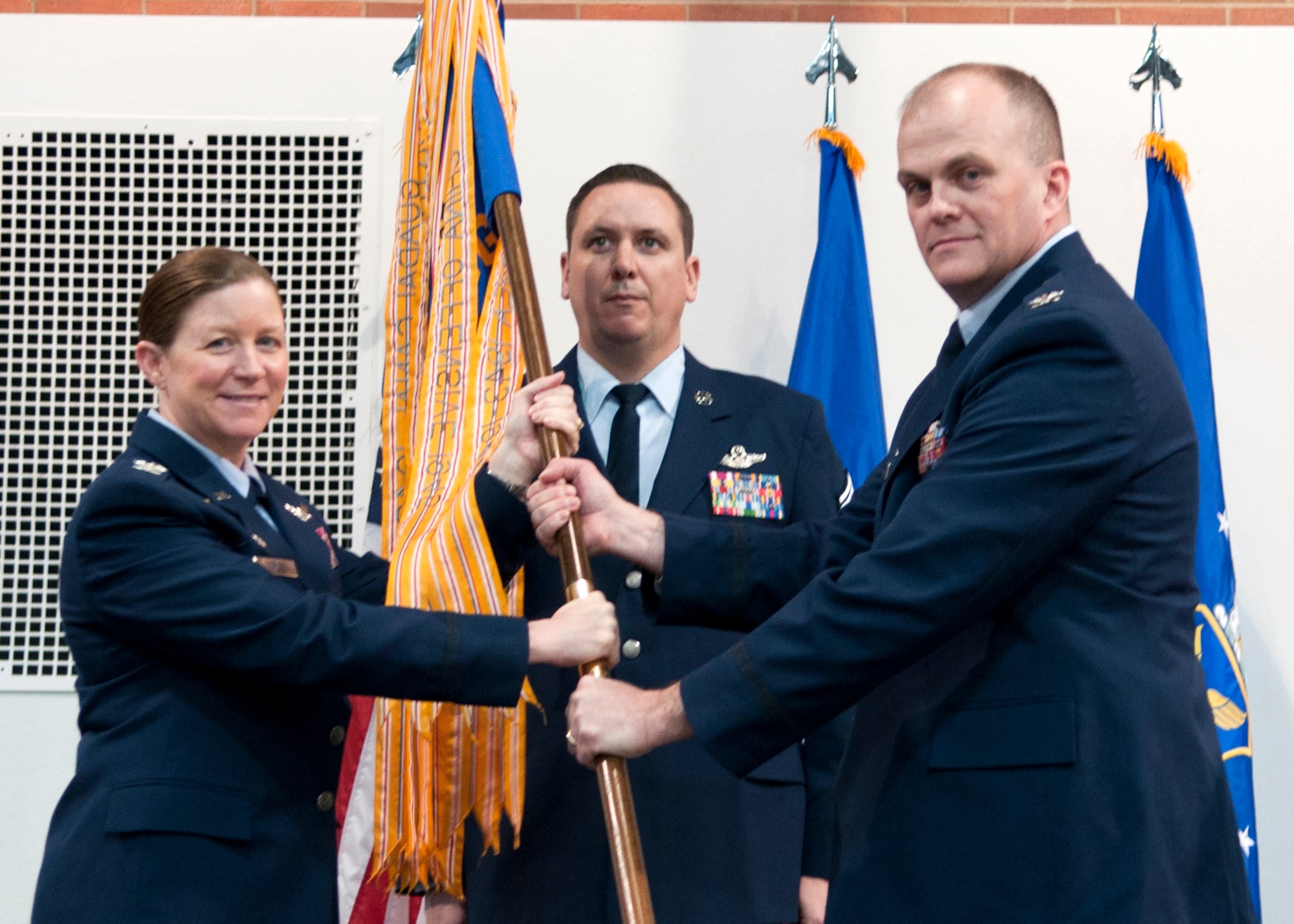 Col. Tracey Hayes, 90th Missile Wing commander, passes the 90th Operations Group guidon to Col. Todd Sauls as he assumes command of the group during a change-of-command ceremony Dec. 3, 2014 in the Fall Hall community center on F.E. Warren Air Force Base, Wyo. Chief Master Sgt. Paul Jacobs, 90th OG superintendent, stands by to take the guidon back from Sauls. (U.S. Air Force photo/ Airman 1st Class Malcolm Mayfield)