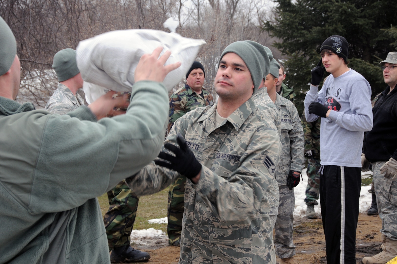 Senior Airman Travis Besette, of the 119th Civil Engineer Squadron, center, catches a sandbag to pass along a human chain of National Guard members March 16, Fargo, N.D. The North Dakota Airmen from the 119th Wing were woven in between local high school student volunteers in sandbag lines that extended from pallets on the street and in driveways, through garages and out back doors. The quickly rising river behind them reminded them of the urgency of their mission.