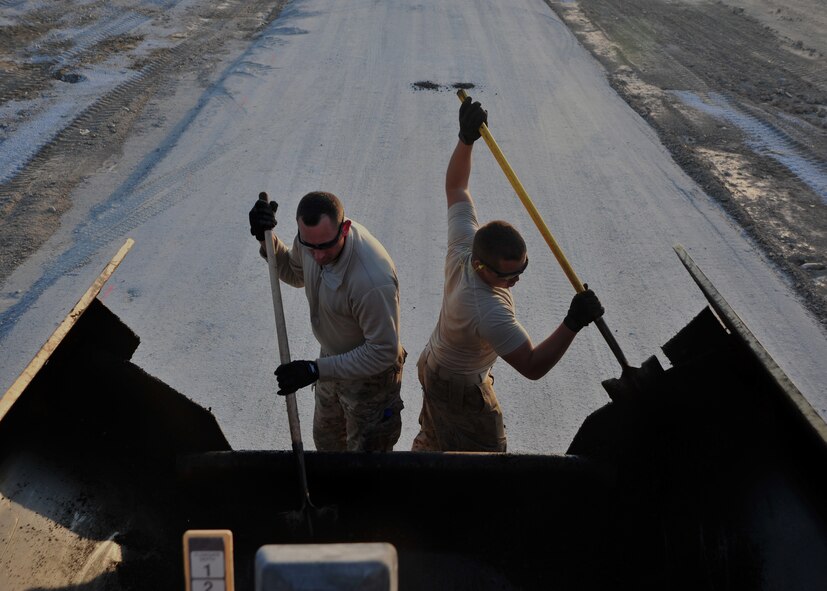 U.S. Air Force Airmen assigned to the 557th Expeditionary Rapid Engineer Deployable Heavy Operational Repair Squadron Engineers (RED HORSE) Squadron, shovel asphalt into the base of a paver Dec. 2, 2014 at Bagram Airfield, Afghanistan. The RED HORSE team travels throughout the region completing high-priority projects to facilitate mission-accomplishment. (U.S. Air Force photo by Staff Sgt. Whitney Amstutz/ released)