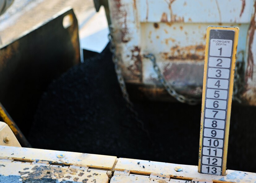 Asphalt pours from a dump truck into the mouth of a paver Dec. 2, 2014 at Bagram Airfield, Afghanistan. Once filtered through the paver, the asphalt is heated and leveled onto the road at temperatures greater than 300 degrees Fahrenheit. (U.S. Air Force photo by Staff Sgt. Whitney Amstutz/ released)