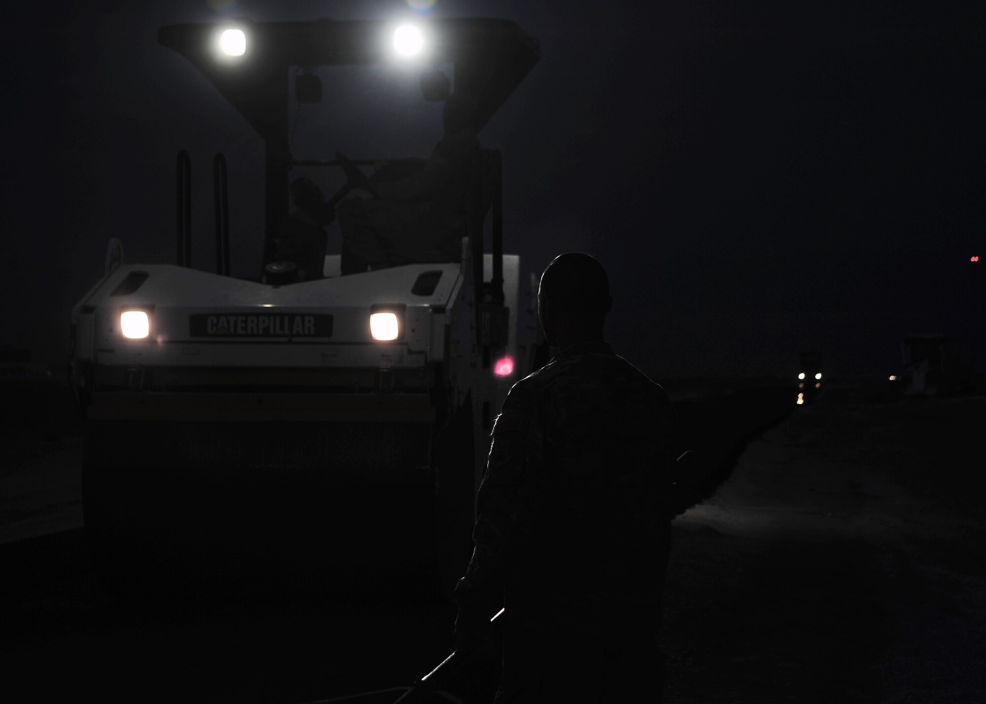 U.S. Air Force Senior Airman Andrew Miculob, 557th Expeditionary Rapid Engineer Deployable Heavy Operational Repair Squadron Engineers (RED HORSE) Squadron pavement and construction, waits with an asphalt rake in hand, as a roller flattens out freshly-laid asphalt Dec. 2, 2014 at Bagram Airfield, Afghanistan. The RED HORSE team worked late into the night in order to complete construction of Ammo Road at the 455th Air Expeditionary Wing. (U.S. Air Force photo by Staff Sgt. Whitney Amstutz/released)