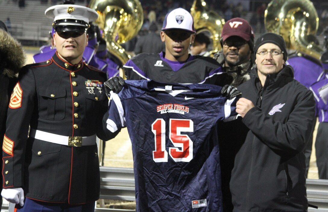 U.S. Marine Corps Gunnery Sgt. Robert Beatty, left, a recruiter with Marine Corps Recruiting Sub Station Greensboro, and Brian Thomas, right, the athletic director for Northern Guilford High School, present Mook Reynolds, a defensive back for the Northern Guilford High School football team, with a jersey during his Semper Fidelis All-American Bowl jersey presentation at Northern Guilford High School in Greensboro, North Carolina, Nov. 14, 2014. Reynolds was selected to play in the bowl for his skill as a defensive back, his academics and his leadership ability.  The Semper Fidelis All-American Bowl allows the Marine Corps to purposefully engage with well-rounded student athletes to share leadership lessons that will enable future success. It will be played on Jan. 4, 2015, in Carson City, Calif., and will be broadcast on Fox Sports 1. (U.S. Marine Corps photo by Sgt. Dwight A. Henderson/Released) 