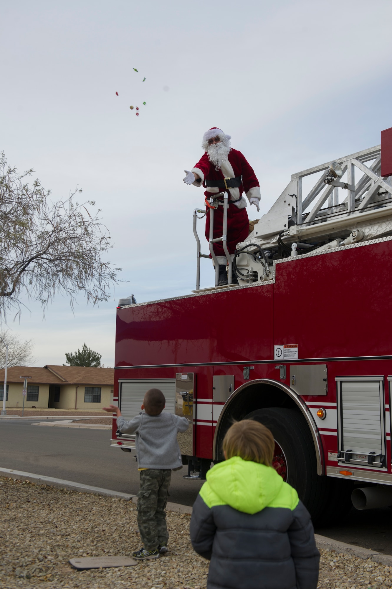 Santa Claus greets children and tosses candy to them before the parade throughout the Soaring Heights housing community at Holloman Air Force Base, N.M., Dec. 2. The 49th Civil Engineer Squadron Fire Protection Flight gave Santa a ride on their fire engine. Members of Team Holloman teamed up to offer various holiday activities for families to enjoy before the Christmas tree lighting ceremony that evening. (U.S. Air Force photo by Airman 1st Class Aaron Montoya / Released)