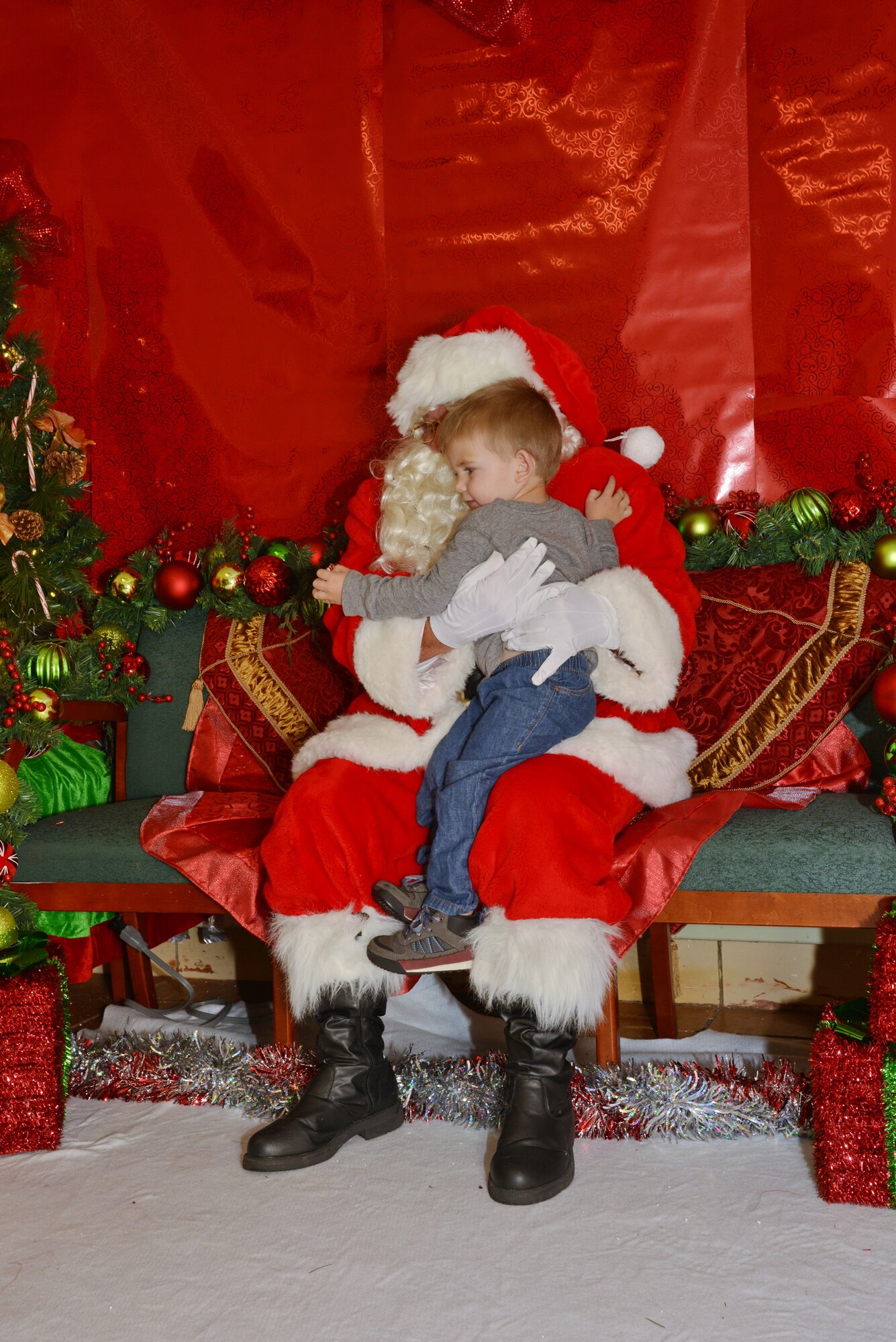 Zach Magnuson gives Santa Claus a giant hug during the Tree Lighting Ceremony at the Base Chapel Dec. 4. All planned festivities were moved inside the chapel due to rainy weather. (Photo by Jamie Burnett)