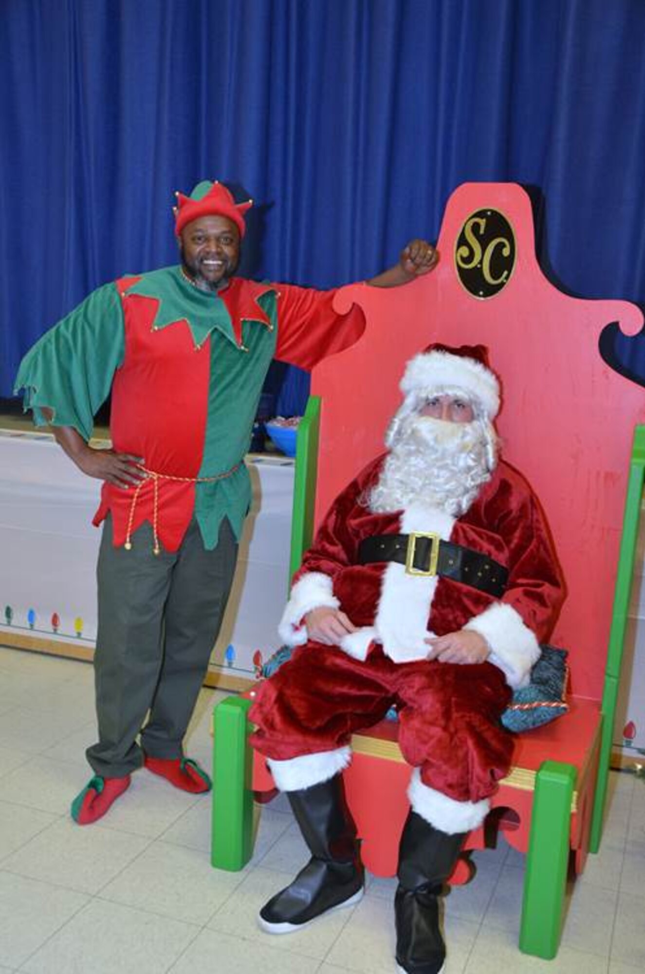 Corvias employees Harvey Bolton (left) and Darryl Cowart (right) wait to greet dozens of military children at the Tis the Season at Branch Elementary Dec. 4.  Besides visiting Santa Claus, children could also build wooden toys, make ornaments, play games and try their luck at a prize wheel at the event. (Courtesy photo by Mark Nettles)