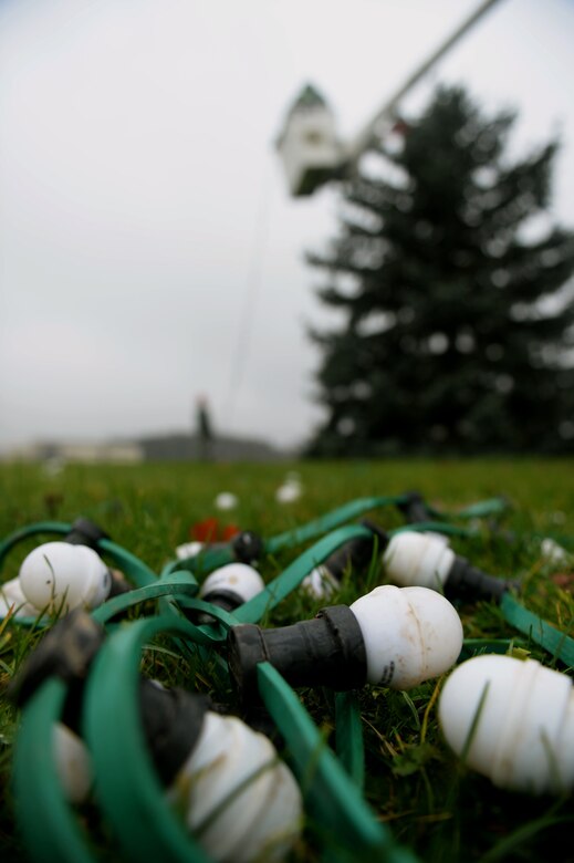 Decoration lights rest on the grass in front of an evergreen tree at the Saber Circle in Spangdahlem Air Base, Germany, Dec. 2, 2014. Airmen used multi-colored lights and cords to decorate the tree. (U.S. Air Force photo by Airman 1st Class Timothy Kim/Released)