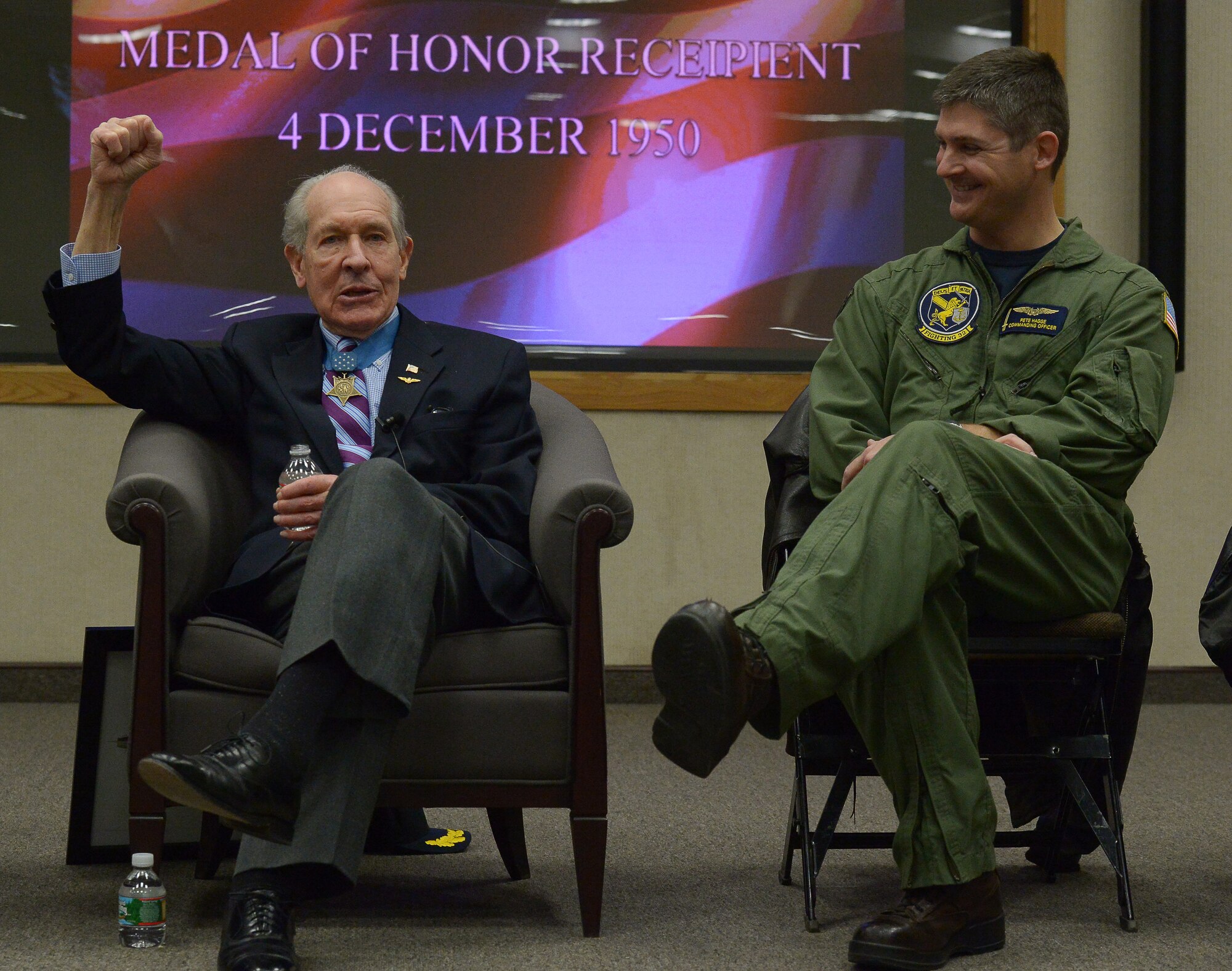 U.S. Navy Commander Peter Hagge, commanding officer of Strike Fighter Squadron 32, smiles as Medal of Honor recipient retired U.S. Navy Capt. Thomas Hudner Jr. tells a humorous story from his flying days during a ceremony in his honor at Hanscom Air Force Base, Mass., Dec. 4, 2014. Hagge is the weapons systems officer of the F-18F Super Hornet that bears the name of Hudner on one side and Ensign Jesse Brown, the pilot Hudner tried to rescue, on the other. SFS 32 is the descendant of the unit Hudner flew with during the Korean War. Hanscom hosted the event on the 64th anniversary of the Korean War actions that earned Hudner his Medal of Honor. (U.S. Air Force photo/Jerry Saslav)