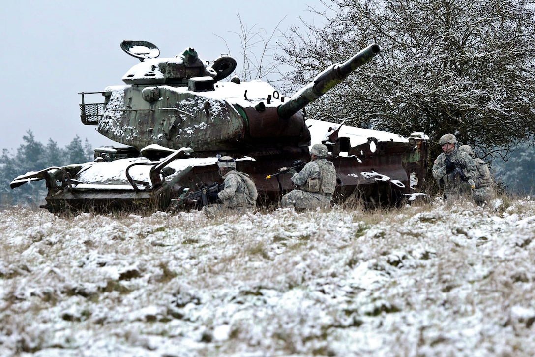U.S. soldiers take cover behind an old tank during a squad fire exercise at Hohenfels Training Area, Germany, Dec. 3, 2014.