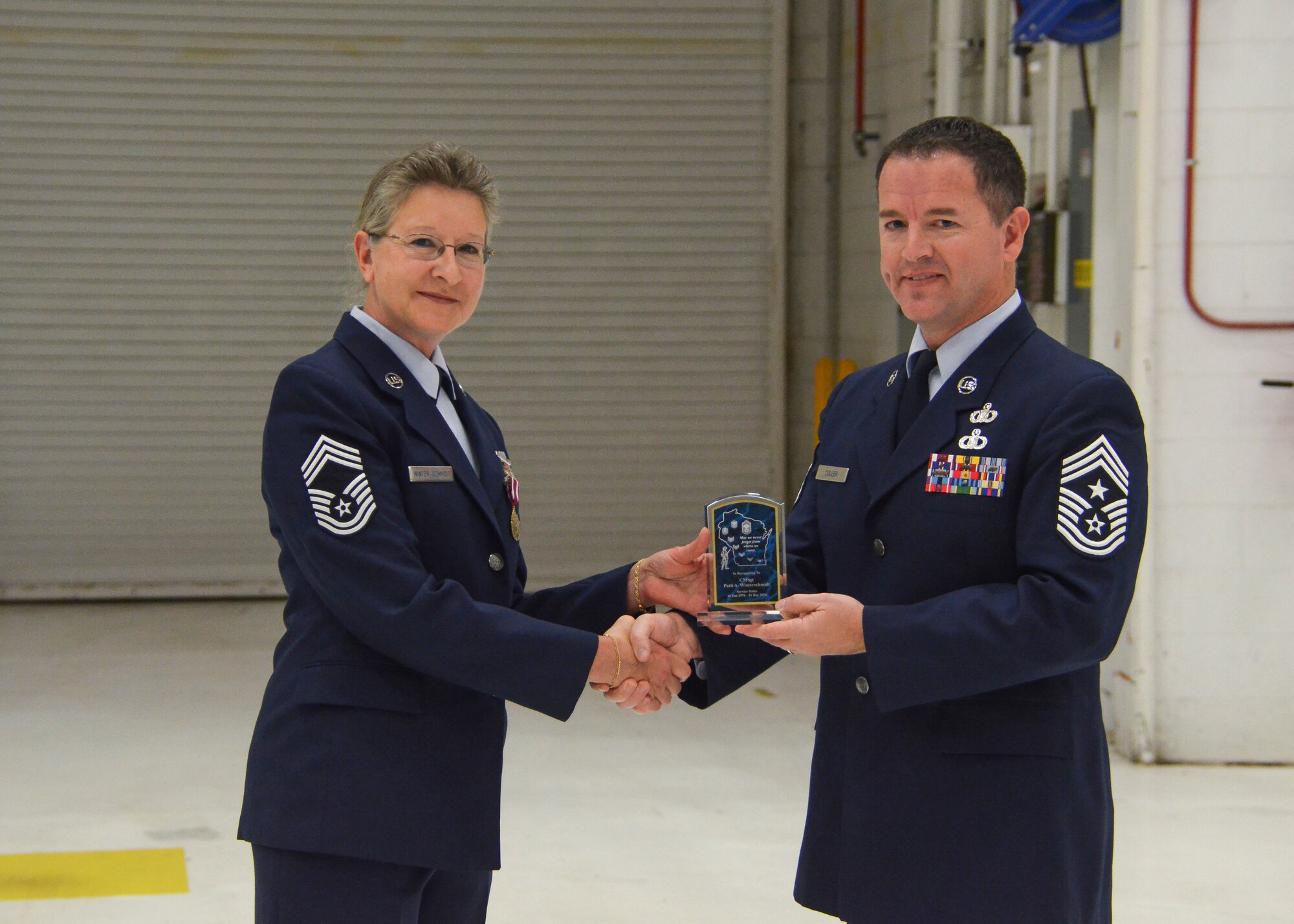 Chief Master Sgt. Greg Cullen, the command chief master sergeant of the State of Wisconsin, presents an award to Chief Master Sgt. Patti Winter-Schmidt during her retirement ceremony in an aircraft hangar here Dec. 7, 2014.  Winter-Schmidt served a 38-year career in the military and was the first female to be promoted to Chief Master Sgt. at the 128 ARW.  (U.S. Air National Guard photo by Master Sgt. Thomas J. Sobczyk/Released)