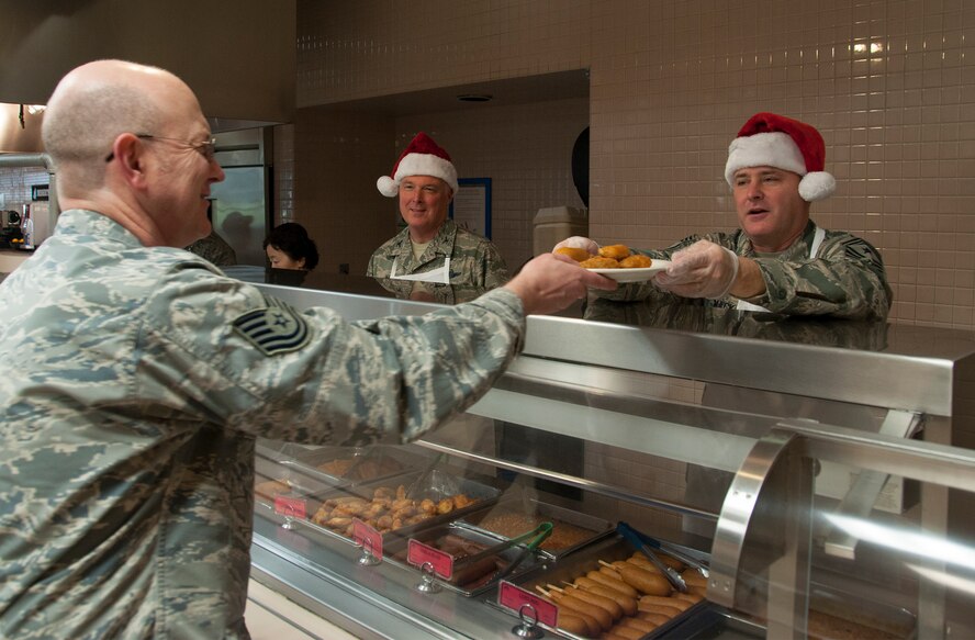 Col. Scott McLaughlin (center), 446th Airlift Wing commander, and Chief Master Sgt. Anthony Mack (right), 446th AW command chief, serve food to Tech. Sgt. Troy Leiker (left), 446th Force Support Squadron formal schools manager, at the Olympic Dining Facility on Dec. 7. In an effort to spread holiday cheer, several officer and enlisted leader throughout the 446th Airlift Wing volunteered their time to help serve lunch during the December unit training assembly weekend. (U.S. Air Force Reserve photo by Staff Sgt. Bryan Hull)
