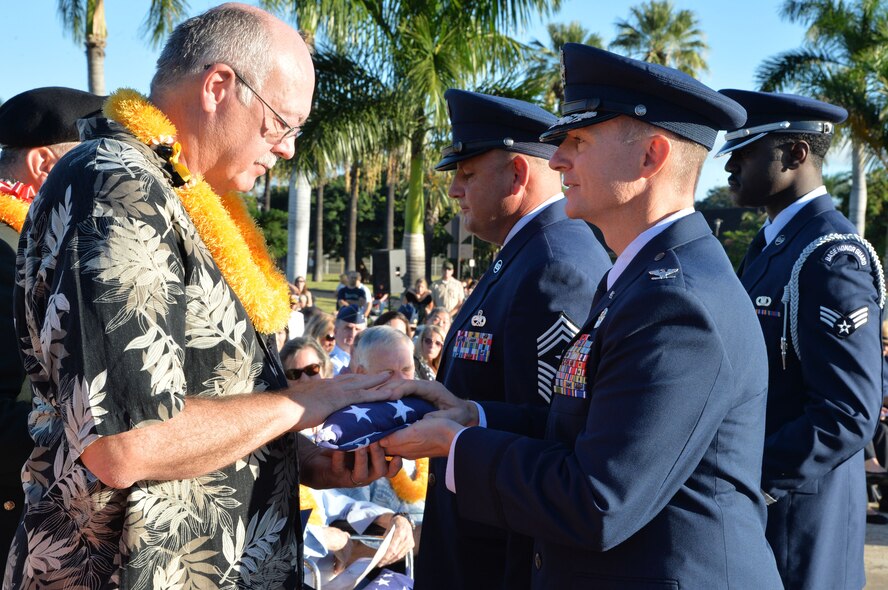 U.S. Air Force Col. Randy Huiss, 15th Wing commander, presents a U.S. flag to Thomas Shepherd, the son of an Army Air Corpsman who survived the attacks on Hickam Field on Dec. 7, 1941, during the Attack on Hickam Field Remembrance Ceremony at Joint Base Pearl Harbor-Hickam, Hawaii Dec. 7, 2014. This year’s ceremony marks 73 years to the day since the attack occurred. More than 50 survivors and family members of survivors attended the ceremony, which honors the 189 Airmen who lost their lives in the attack. (U.S. Air Force photo by Staff Sgt. Alexander Martinez/Released)