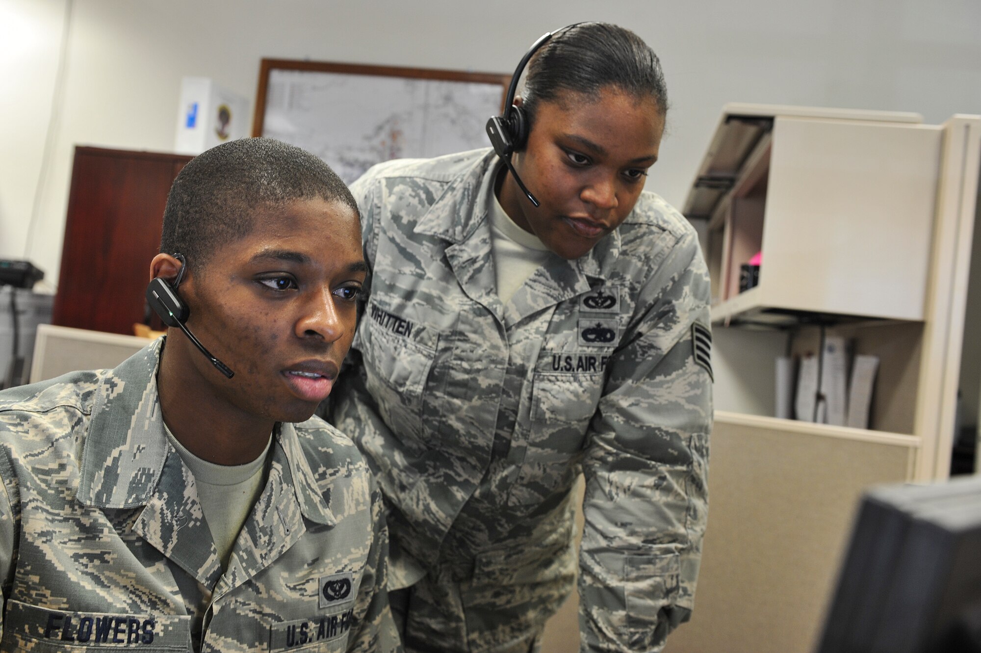 Staff Sgt. Konisha Whitten, 1st Special Operations Civil Engineer Squadron operations management, guides Airman 1st Class Charles Flowers, 1st SOCES civil engineer journeyman, through a work order submission at the “Fish Bowl” on Hurlburt Field, Fla., Dec. 4, 2014. Airmen at the Fish Bowl take calls and create work orders for various shops at the 1st SOCES to complete around the base. (U.S. Air Force photo/Airman 1st Class Jeff Parkinson)