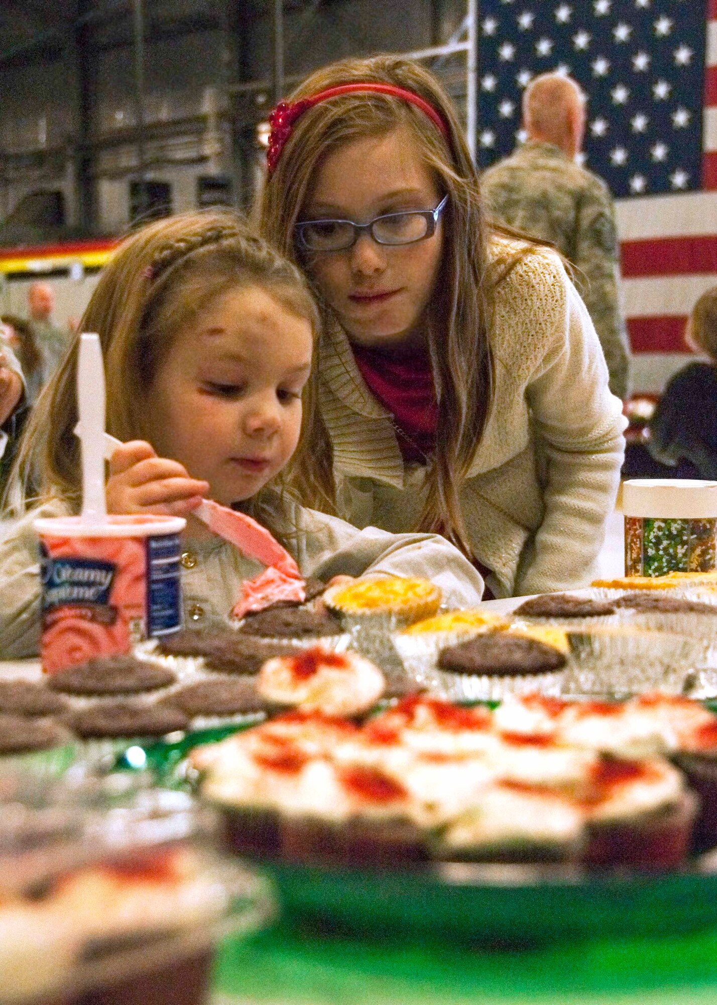While awaiting Santa’s arrival, Gabriella McCleskey, age 4, frosts cupcakes as her older sister, Caitlyn Wright, age 12, lends a helping hand.  (U.S. Air Force photo/Staff Sgt. Crystal Charriere) 