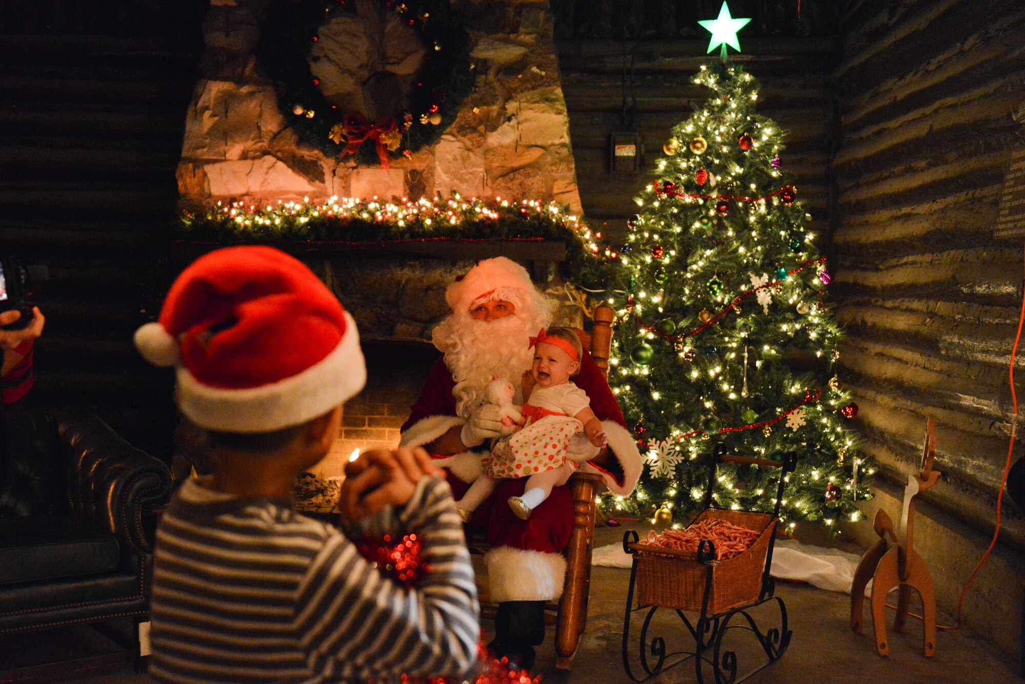 Son of Tech. Sgt. Triscia Garcia, 334th Training Squadron, watches as the daughter of Senior Airman Thomas Miller, 305th Maintenance Squadron, experiences her first Christmas on Santa's lap during Christmas iIn tThe Park Dec. 3, 2014, at Marina Park, Keesler Air Force Base, Miss. The event, hosted by Outdoor Recreation, included a tree lighting ceremony, hay rides, holiday music, cookie decorating and visits with Santa. (U.S. Air Force photo by Marie Floyd)