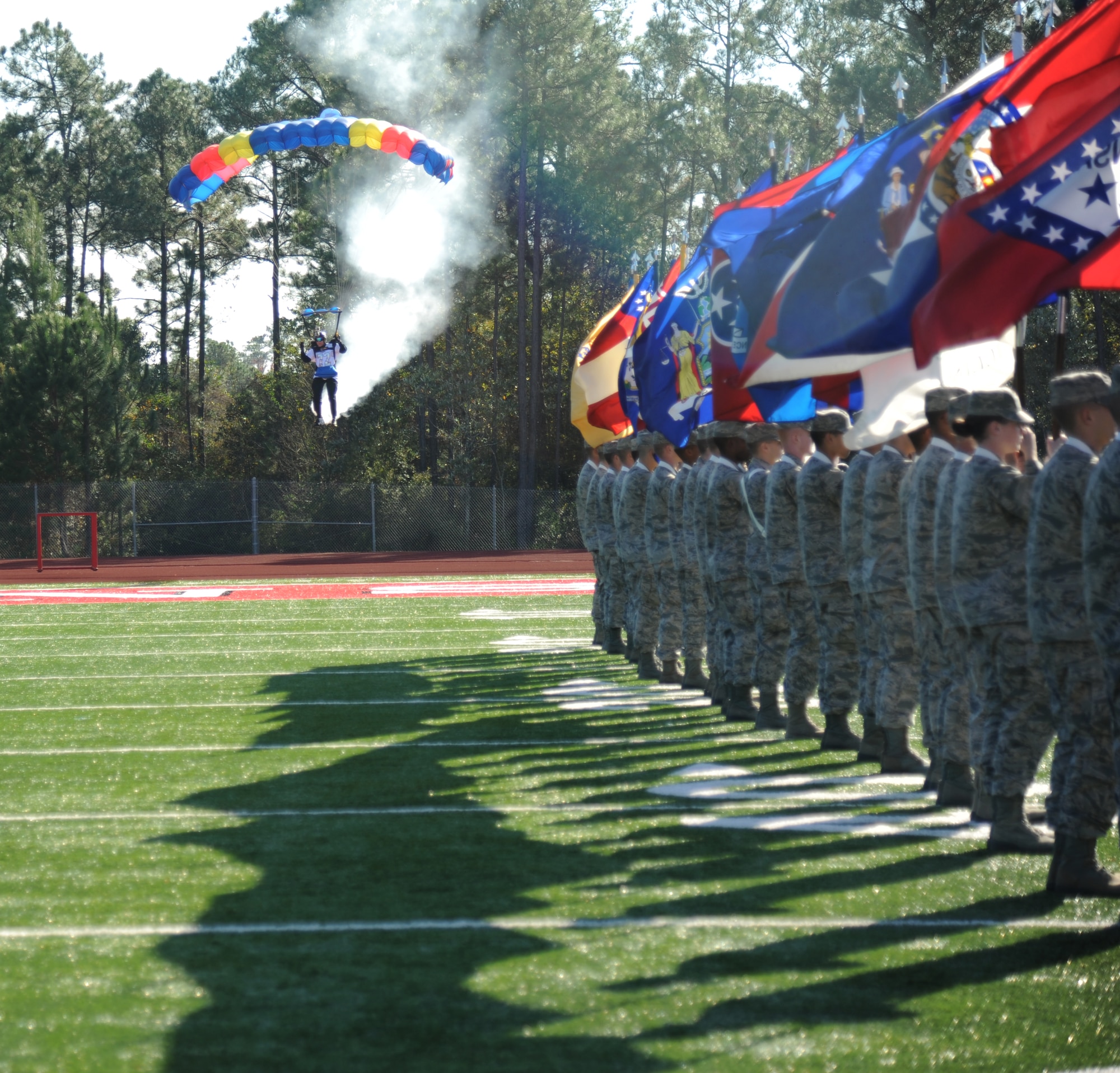 Greg Bryant, American Skydiving Team, prepares to land on the field behind Airmen carrying the 50-State flags during the 2014 Mississippi Bowl Dec. 7, 2014, at the Biloxi High School Football Stadium. Brig. Gen. Patrick Higby, 81st Training Wing commander, and the Keesler Honor Guard also participated in the pre-game celebration. (U.S. Air Force photo by Kemberly Groue)