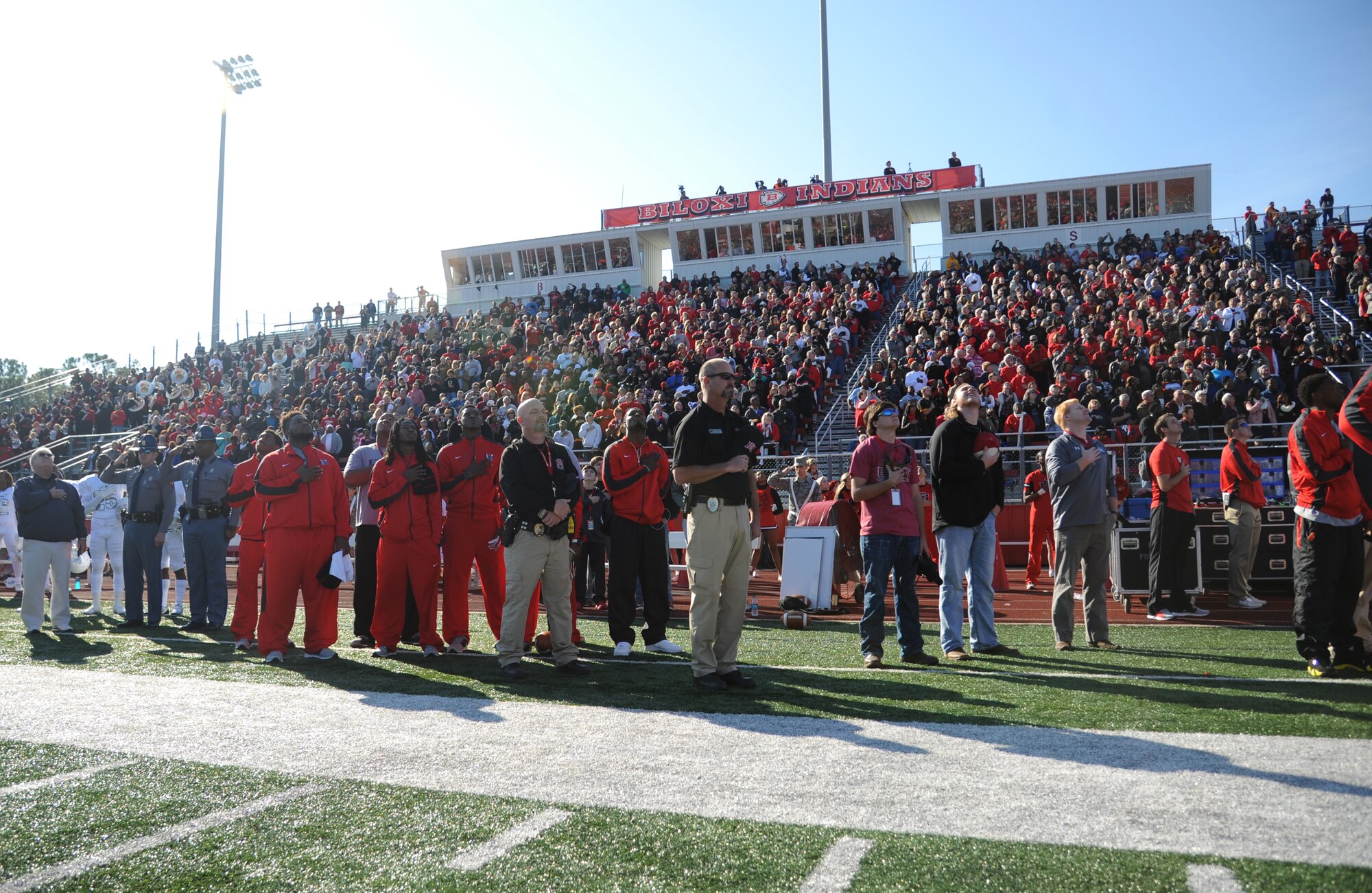 Coaches, football players and spectators look to the sky as an American Skydiving Team member parachutes down with the U.S. flag as the National Anthem is sung during the 2014 Mississippi Bowl Dec. 7, 2014, at the Biloxi High School Football Stadium. Senior Airman Robert DeSantis, 81st Medical Group aerospace medical technician, sang the National Anthem. (U.S. Air Force photo by Kemberly Groue)