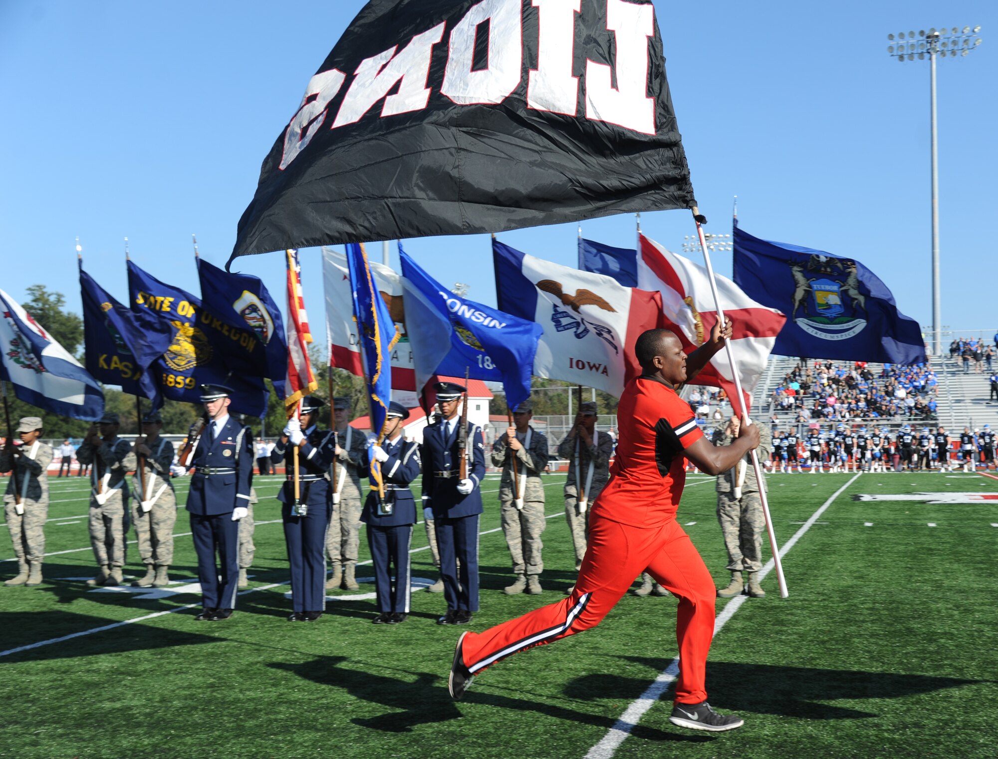 Nolin Collymore, East Mississippi Community College cheerleader, leads his football team onto the field carrying the “Lions” flag during the 2014 Mississippi Bowl Dec. 7, 2014, at the Biloxi High School Football Stadium. The Keesler Honor Guard and Airmen carrying the 50-State flags participated in the pre-game celebration. (U.S. Air Force photo by Kemberly Groue)
