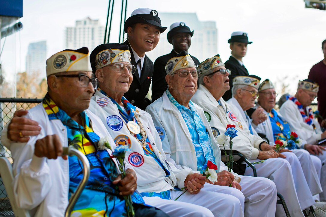 Sailors pose for a photo with honorary members of the Pearl Harbor Survivors Association, Chapter 3, toss a reef during a remembrance ceremony for the 73rd anniversary of the attack on Pearl Harbor aboard the USS Midway Museum in San Diego, Dec. 7, 2014.