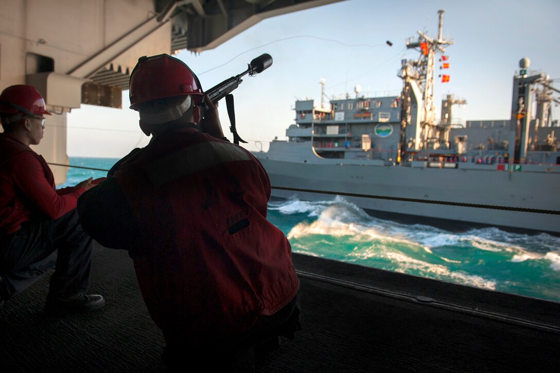 U.S. Navy Seaman Robert Cruz, a gunner's mate, fires a shot line from the hangar bay of the Nimitz-class aircraft carrier USS Carl Vinson to the Military Sealift Command fast combat support ship USNS Rainier during a replenishment-at-sea operation in the Arabian Gulf, Dec. 3, 2014.