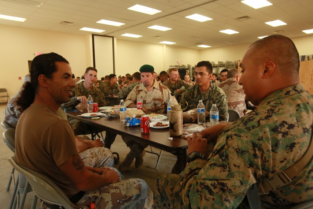 U.S. Marine Corps Gunnery Sgt. Michael Ramirez with Battalion Landing Team 3rd Battalion, 1st Marine Regiment, 15th Marine Expeditionary Unit, shares a meal with role-players while participating in realistic urban training aboard Fort Hunter Liggett, Calif., Dec. 8, 2014. The Marines were simulating bi-lateral training exercises they could be tasked with while deployed. RUT prepares the 15th MEU's Marines for their upcoming deployment, enhancing their combat skills in environments similar to those they may find in future missions. (U.S. Marine Corps Photo by Sgt. Jamean Berry/Released)