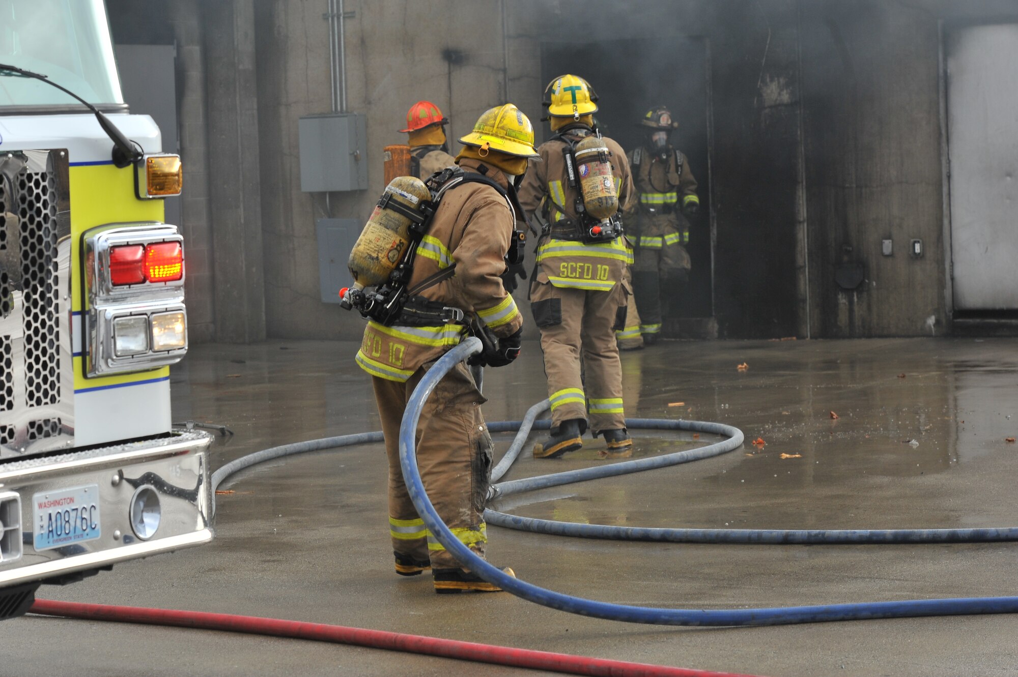 Firefighting recruits from Fairchild Air Force Base, Wash., and the local community spray water into a smoking building during a multi-company training drill Dec. 6, 2014, in Spokane Valley, Wash.  Twenty three recruits from the West Plains Fire Academy participated in the all-day training were they ran into a burning building and simulated saving victims. (U.S. Air Force photo/Staff Sgt. Veronica Montes)