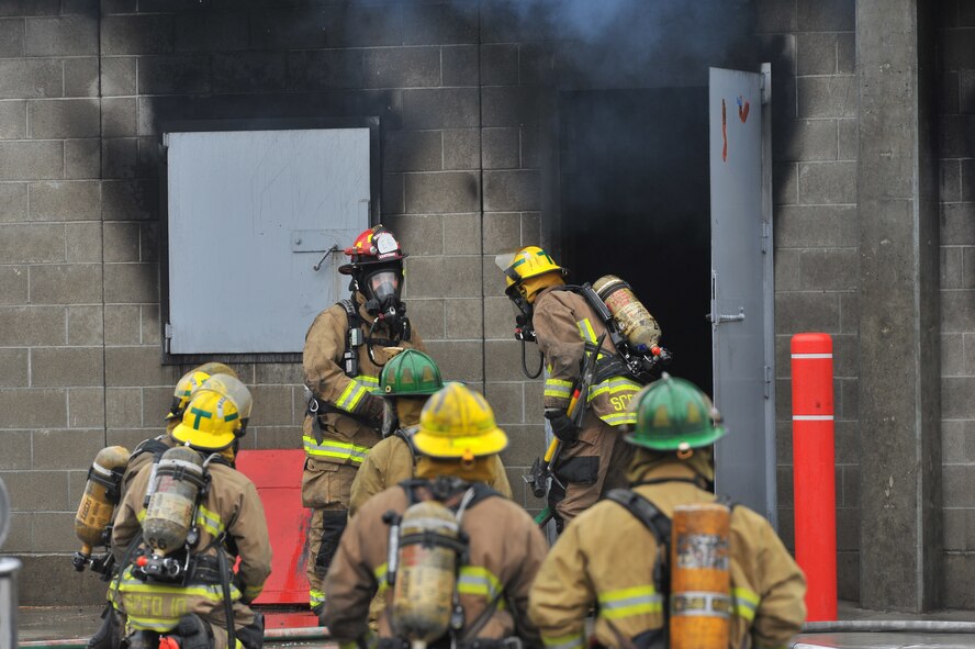 Firefighting recruits from Fairchild Air Force Base, Wash., and the local community enter a smoking building during a multi-company training drill Dec. 6, 2014, in Spokane Valley, Wash.  The 23 recruits participating were part of a four month curriculum conducted by the West Plains Fire Academy.  District 10, Airway heights and Medical Lake stations were part of the all-day training. (U.S. Air Force photo/Staff Sgt. Veronica Montes)