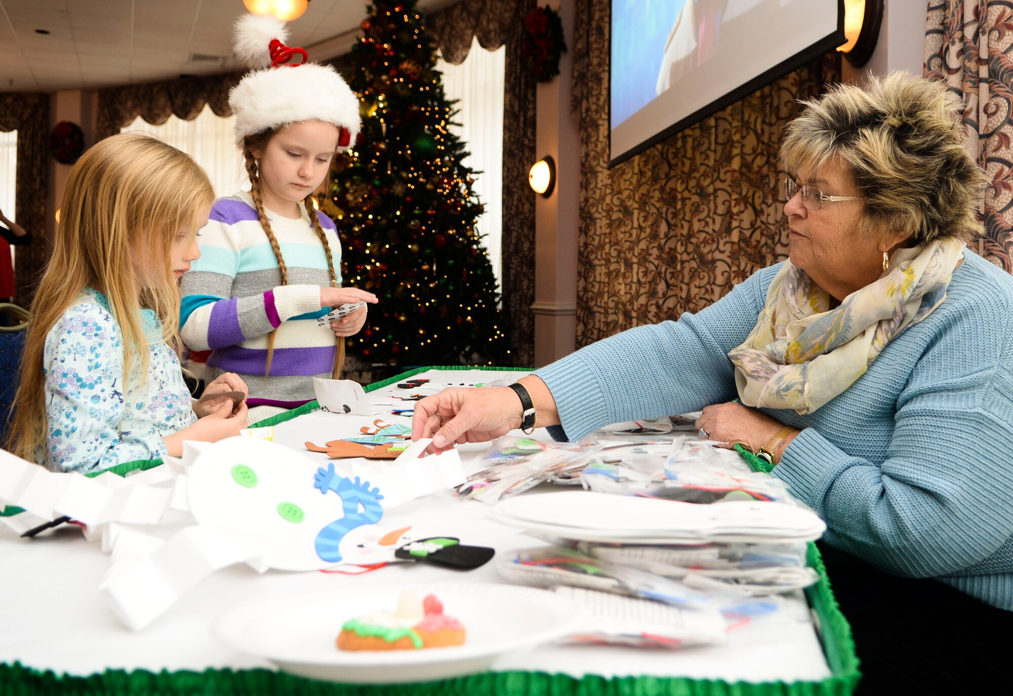 Sherri Noland, 733rd Force Support Division marketing specialist, helps kids make decorations during Breakfast with Santa at Fort Eustis, Va., Dec. 6, 2014. Children could make multiple designs and take their creations home in time for the holidays. (U.S. Air Force photo by Senior Airman Austin Harvill/Released)