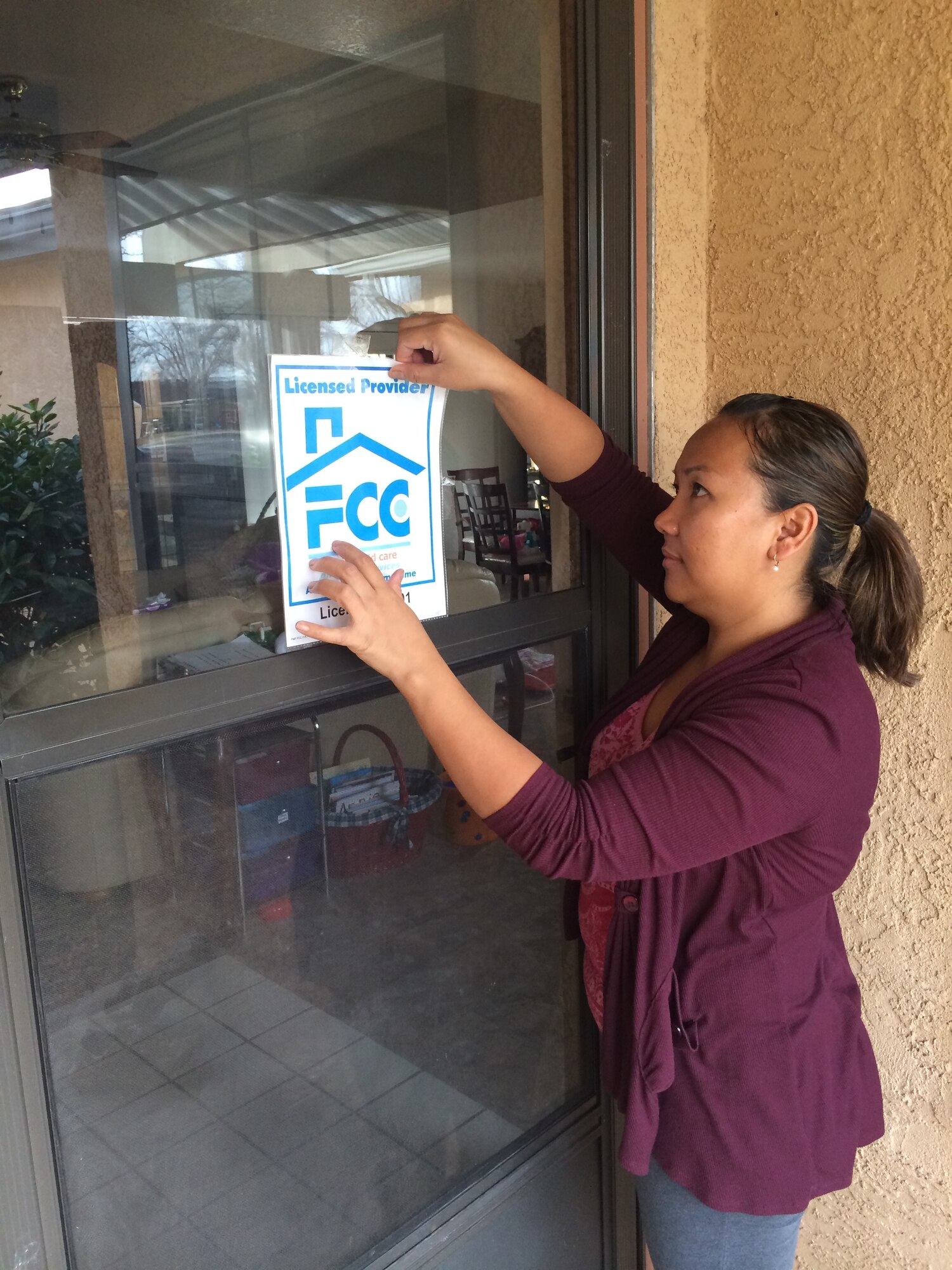 Marie Stabe, 2014 Air Force Materiel Command Family Child Care Provider of the Year, posts her FCC provider sign in the window of her new residence in base housing Dec. 8. Stabe, who was lauded for her above and beyond achievement as an FCC provider, also changed residences in Kirtland Family Housing over the weekend. The provider sign signifies a provider has completed a thorough battery of training, inspections and certification as a licensed FCC provider. (Photo by Tech Sgt. Lucas Stabe)
