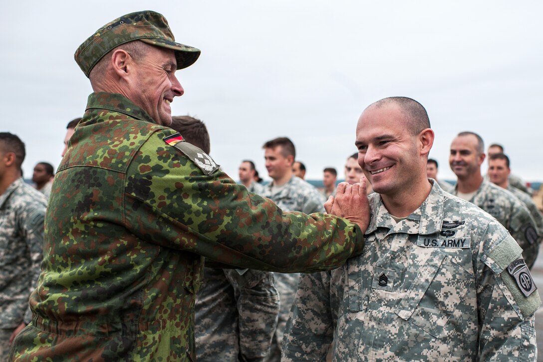 German Army Lt. Col. Andreas Wichert, left, liaison officer to the 18th Airborne Corps, "pins" German jump wings on Army Sgt. 1st Class Shane Weigel at Sicily Drop Zone for the 17th Annual Randy Oler Memorial Operation Toy Drop on Fort Bragg, N.C., Dec. 6, 2014. For Weigel, assigned to the 82nd Airborne Division's 1st Battalion, 508th Parachute Infantry Regiment, it was his third set of German jump wings.