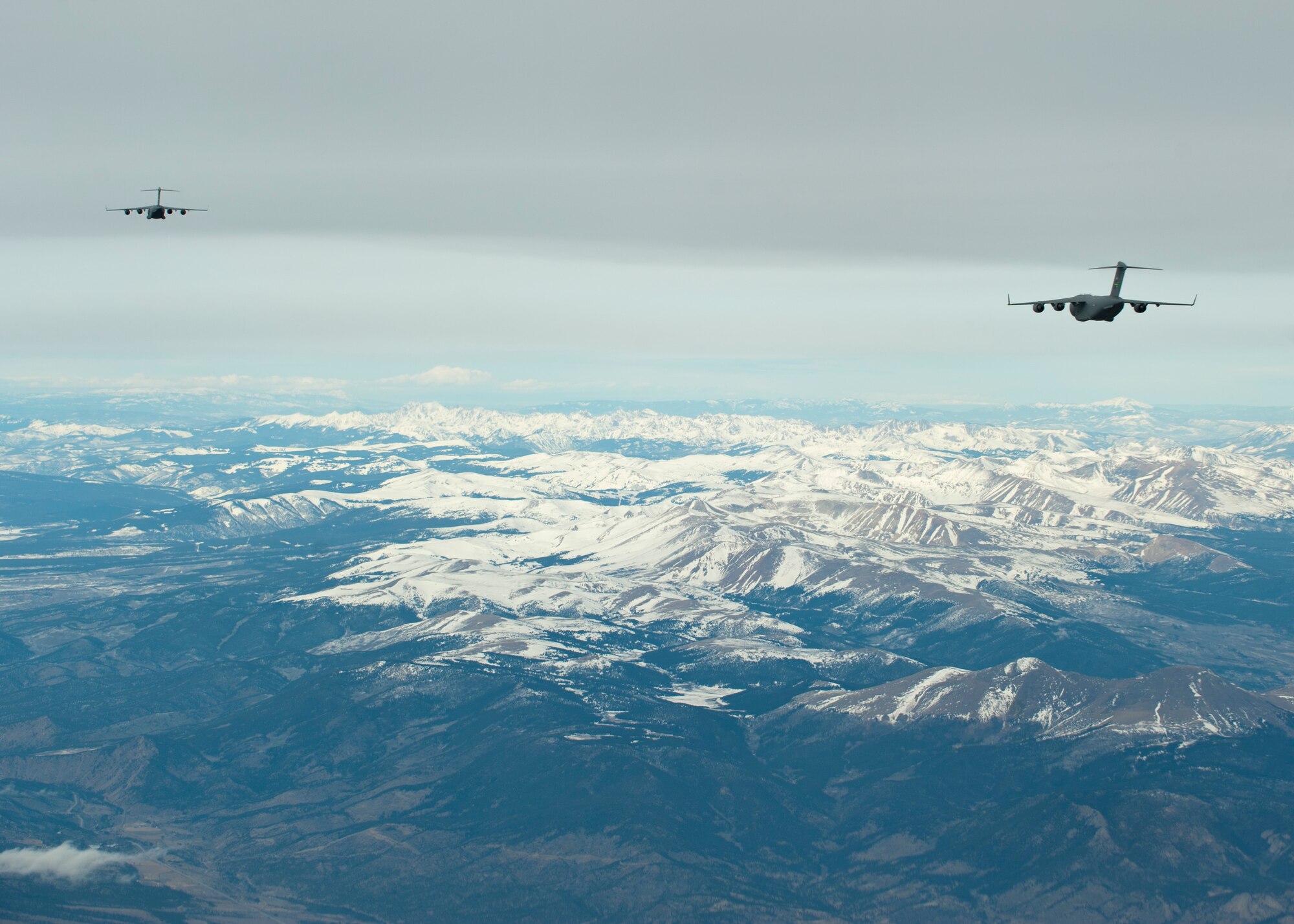 Two U.S. Air Force C-17 Globemaster IIIs fly in formation over the Rocky Mountains en route to the Nevada Test and Training Range to participate in the U.S. Air Force Weapons School's Joint Forcible Entry Exercise 14B Dec. 6, 2014. JFEX, a USAFWS large-scale air mobility exercise, challenges students to plan and execute a complex air-land operation in a simulated contested battlefield. (U.S. Air Force photo by Senior Airman Thomas Spangler)