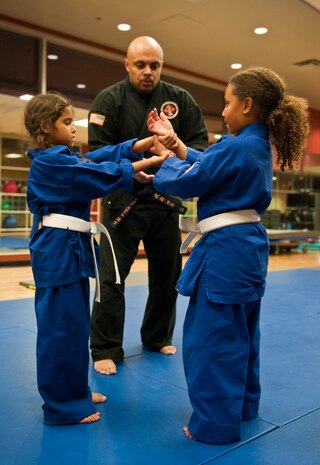 Renshi DeAndre Scott shows Ava and McKenzie correct hand positions during the Nesei Bujutsu class at the Warrior Fitness Center on Nellis Air Force Base, Nev., Dec. 9, 2014. The class focuses on the use of pressure points and minimal force to get the most effect for self-defense. (U.S. Air Force photo by Staff Sgt. Victoria Sneed)