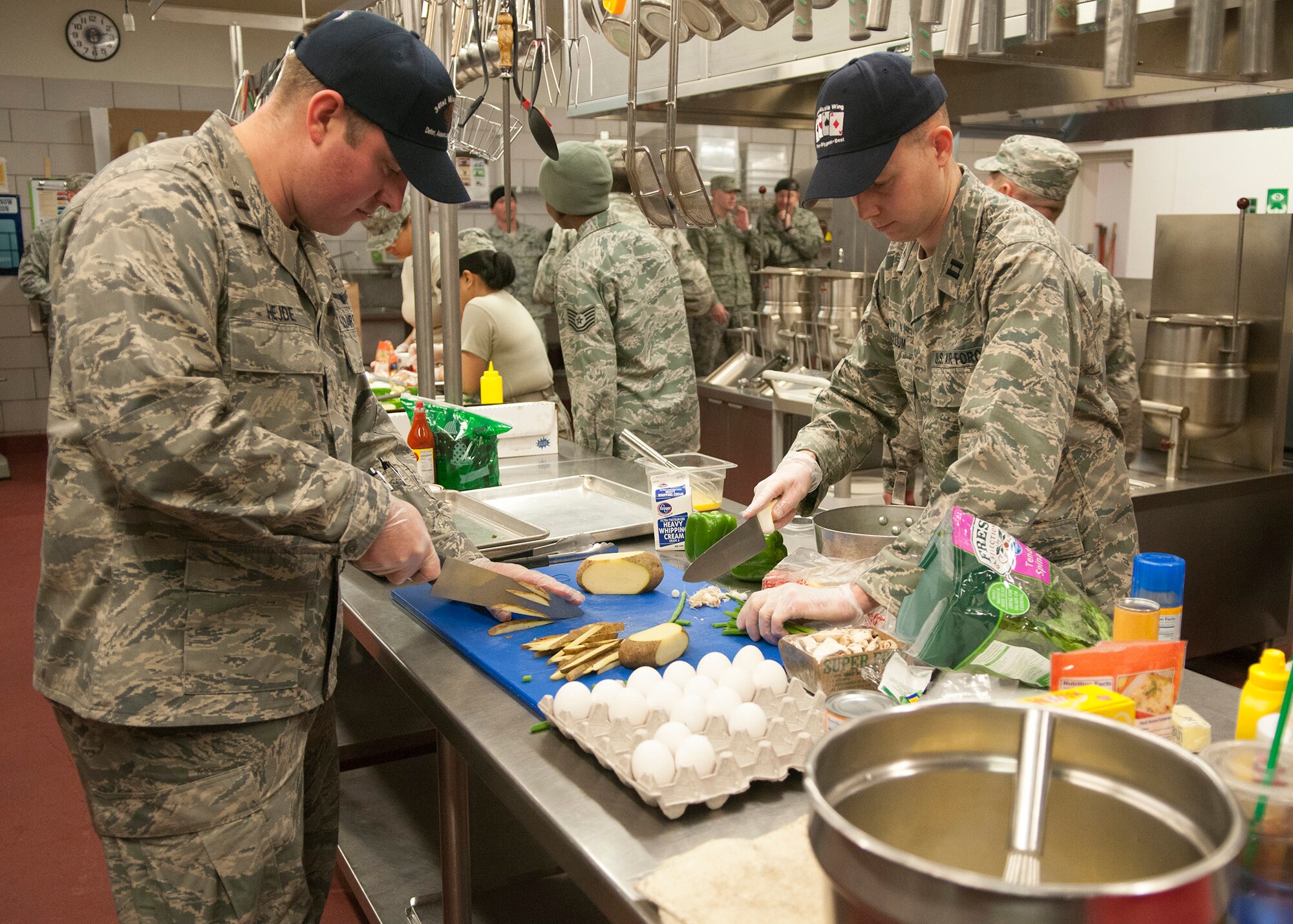 Capts. Daniel Hejde and Chris McCollum, both missile officers from the 341st Operations Group, work as a team Dec. 4 to complete an entrée for the Fourth Quarter Warrior Chef Competition. Two of the five Warrior Chef teams this quarter were from outside the Services career field, representing a new approach to diversifying the competition. (U.S. Air Force photo/Tech. Sgt. Christina Perchine)