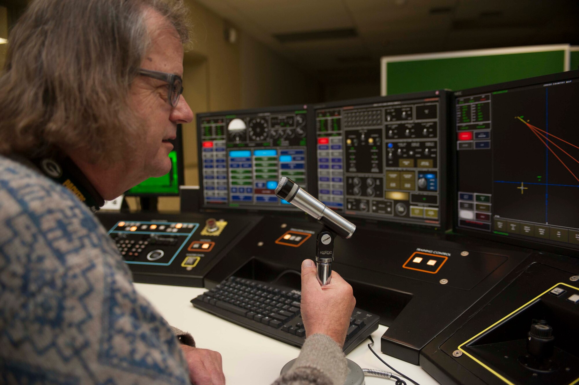 James Wuensch, 5th Operations Support Squadron contractor and system operator, uses a desk microphone to communicate with personnel in the B52-H Stratofortress weapons system trainer on Minot Air Force Base, N.D., Dec. 3, 2014. Wuensch is one of 12 civilian contractors who work to maintain and operate the WST for base aircrews. (U.S. Air Force photo/Senior Airman Stephanie Morris)