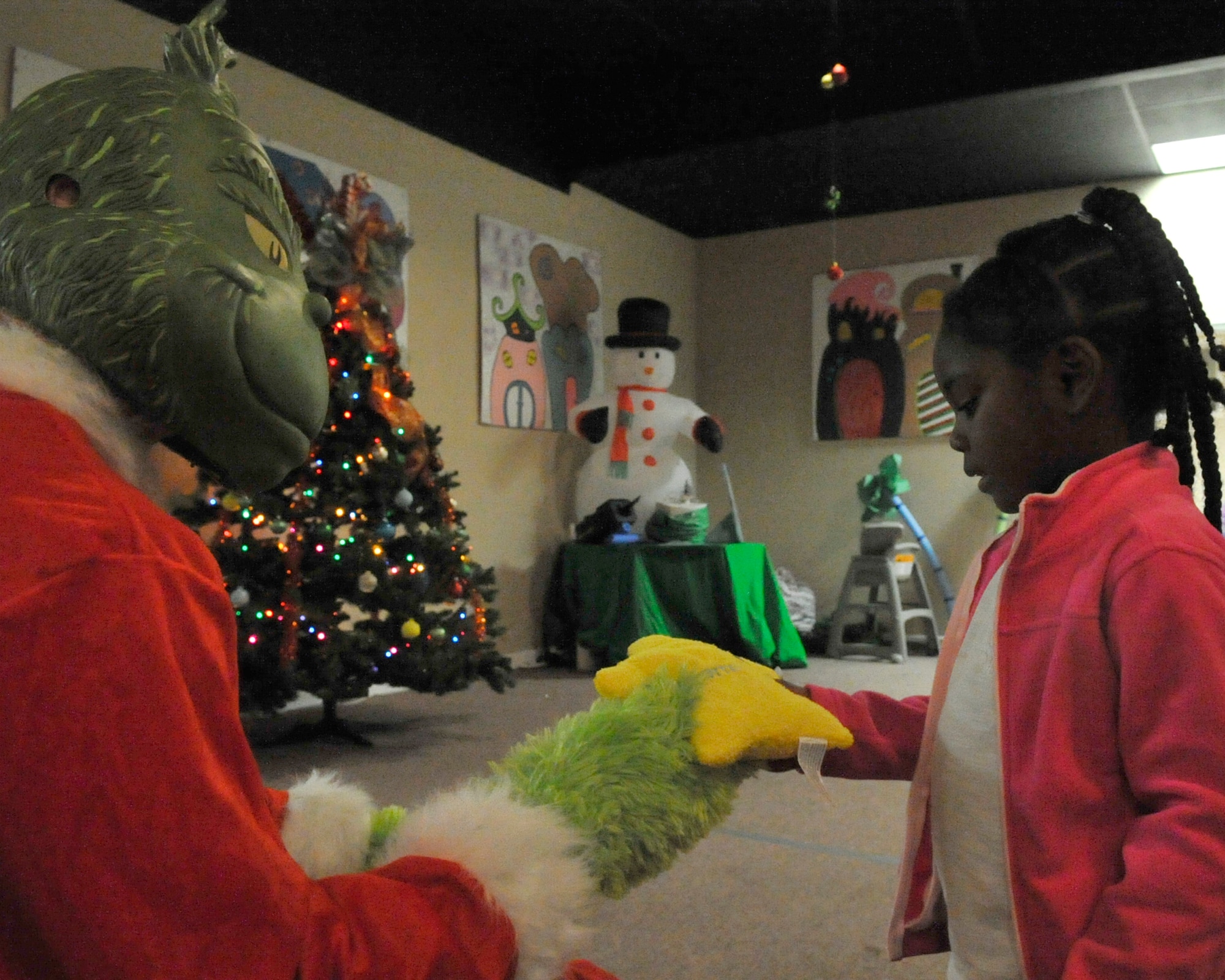 Tatiana Tuft, child of Staff Sgt. Jhoanna, 325th Maintenance Squadron assistant NCO programs flight and Senior Airman Ian Tuft, 325th MXS non-destructive inspection journeyman, receives a gift from Staff Sgt. Michael Dawson, 325th MXS munitions inspector, dressed as The Grinch Dec. 5 at the Hearts Apart Who-liday Party. Dawson volunteered to present gifts to all children in attendance. (U.S. Air Force photo by Airman 1st Class Ty-Rico Lea)