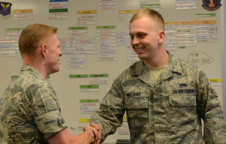 Airman 1st Class Houston Williams, 5th Maintenance Squadron crew chief, reacts to hearing that he has been selected for Operation: Bright Holidays from Capt. Richard Landsverk 5th Operations Support Squadron weather flight commander and Company Grade Officer Council member. The program is designed to help Airmen get home for the holidays. The program, started by the CGOC, began at Minot Air Force Base in 2013, and assists Airmen who may not be able to afford the trip on their own. (U.S. Air Force photo/Airman 1st Class Lauren Pitts)  