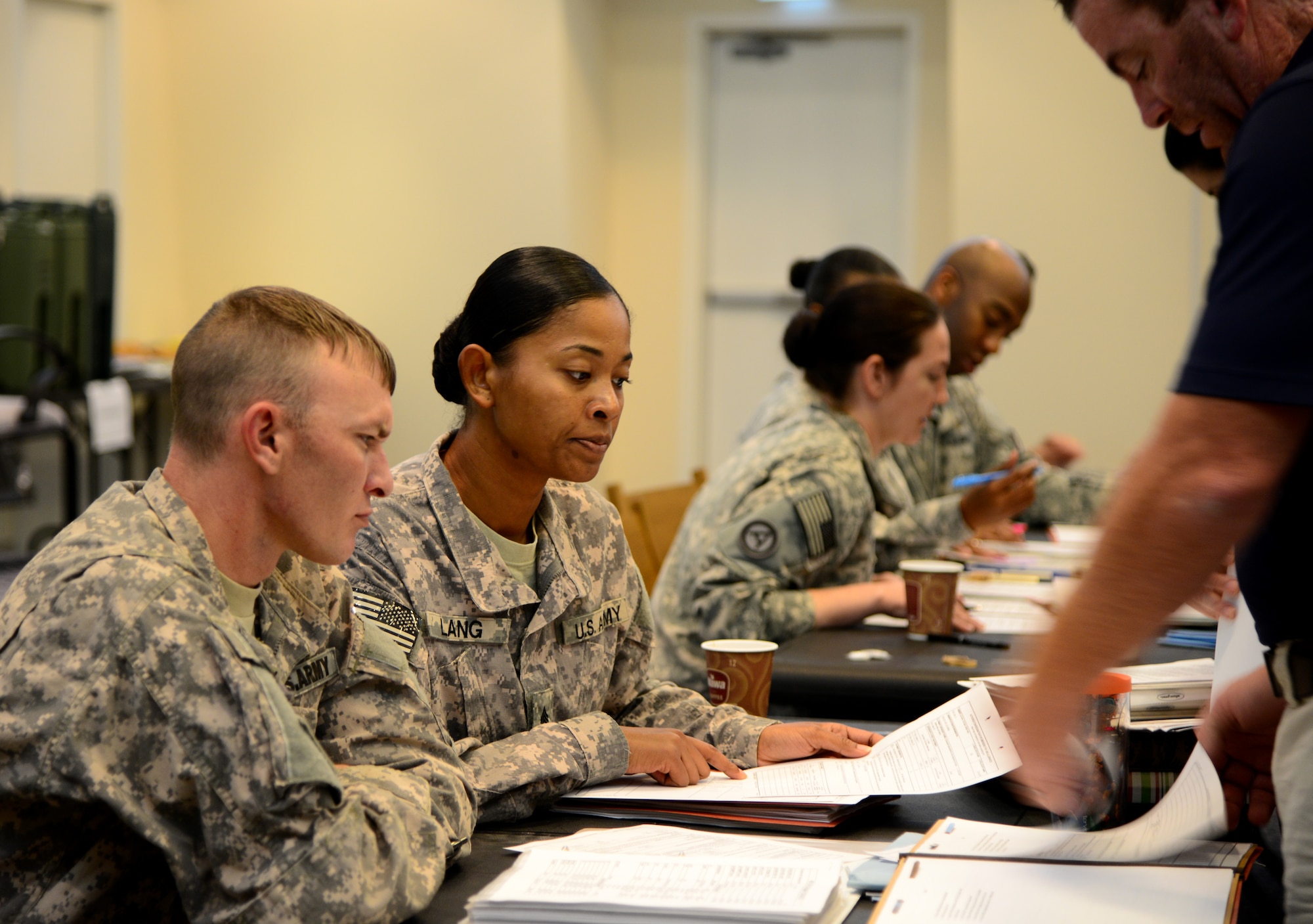U.S. Army Sgt. Sheena Lang, center, Area Support Group-Qatar finance, helps participants of a Noncombatant Evacuation Operations exercise fill out paperwork, Dec. 6, 2014, at Camp As Sayliyah, Qatar. The exercise allowed noncombatants and military members from the Air Force and Army to rehearse evacuation procedures in the event of an emergency in the host nation. (U.S. Air Force photo by Senior Airman Kia Atkins)