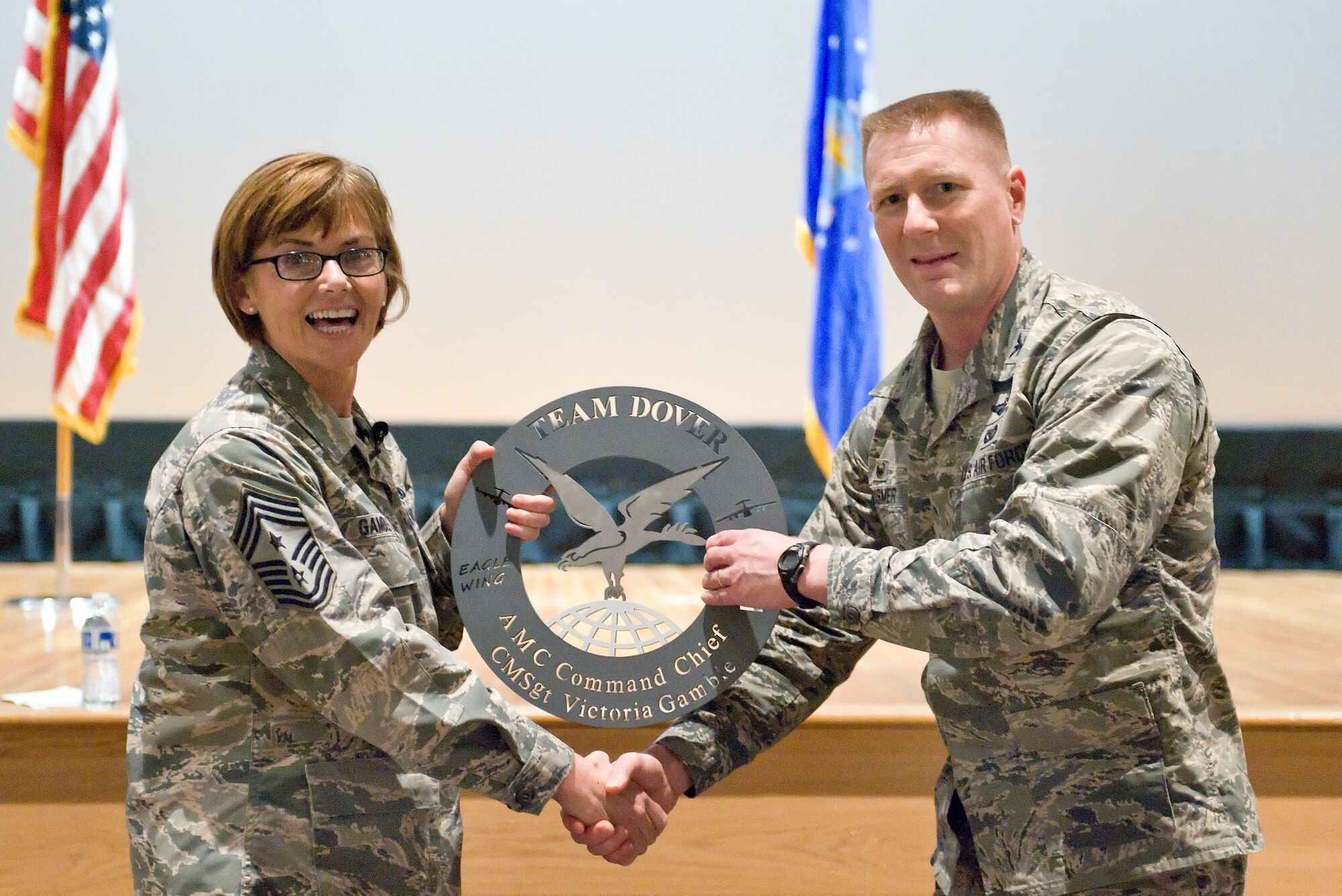 Col. Michael Grismer, 436th Airlift Wing commander, right, presents Chief Master Sgt. Victoria Gamble, Air Mobility Command chief, left, the “Dover Disc” Dec. 4, 2014, at the Base Theater on Dover Air Force Base, Del. Grismer presented Gamble with the disc and a wing coin at the end of an all call as a token of appreciation for talking and visiting with Team Dover members. (U.S. Air Force photo/Roland Balik)
