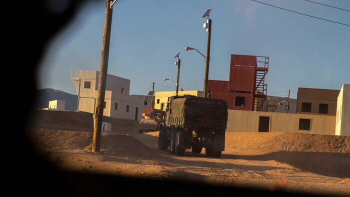 A convoy attached to Truck Company, Combat Logistics Battalion 5, enters a mock enemy town where Marines acting as enemy soldiers waited to ambush the vehicles during convoy training in support of Exercise Steel Knight 2015 at Marine Corps Air Ground Combat Center Twentynine Palms, Calif., Dec. 5, 2014. The exercise gave the Marines the opportunity to refine and rehearse essential combat skills needed in a combat environment. Steel Knight is an annual exercise that includes elements from the entire I Marine Expeditionary Force. The exercise focuses on conventional operations and provides realistic training that prepares Marine for overseas operations. (U.S. Marine Corps photo by Cpl. Christopher J. Moore/Released)