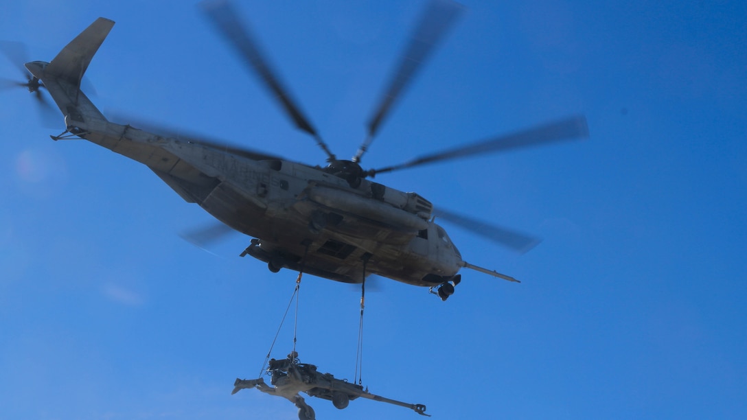 A CH-53E Super Stallion carries an M777 Howitzer that Marines with Landing Support Platoon, Truck Support Company, Combat Logistics Battalion 5, attached to the helicopter as it hovered above them during Exercise Steel Knight 2015 at Marine Corps Air Ground Combat Center Twenty-nine Palms, Calif., Dec. 9, 2014. The exercise gave the Marines the opportunity to refine and rehearse essential skills needed in a combat environment. Steel Knight is an annual exercise that includes elements from the entire I Marine Expeditionary Force. The exercise focuses on conventional operations and provides realistic training that prepares Marine for overseas operations. (U.S. Marine Corps photo by Cpl. Christopher J. Moore/Released)
