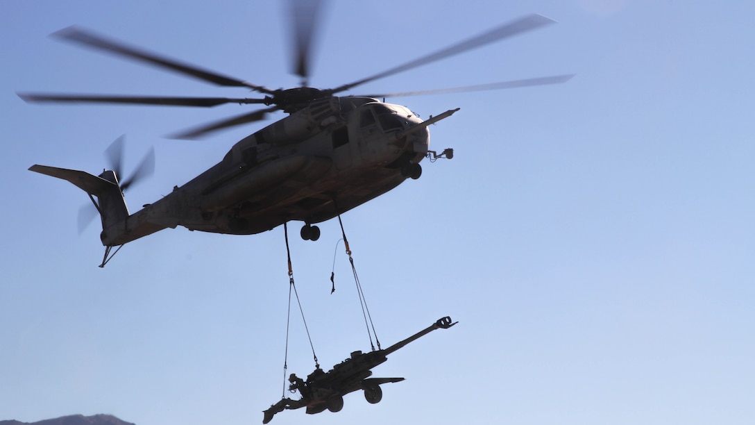 A CH-53E Super Stallion carries an M777 Howitzer that Marines with Landing Support Platoon, Truck Support Company, Combat Logistics Battalion 5, attached to the helicopter as it hovered above them during Exercise Steel Knight 2015 at Marine Corps Air Ground Combat Center Twenty-nine Palms, Calif., Dec. 9, 2014. The exercise gave the Marines the opportunity to refine and rehearse essential skills needed in a combat environment. Steel Knight is an annual exercise that includes elements from the entire I Marine Expeditionary Force. The exercise focuses on conventional operation and provides realistic training that prepares Marine for overseas operations. (U.S. Marine Corps photo by Cpl. Christopher J. Moore/Released)