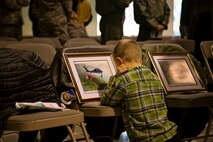 Elias Watson, six year-old son of Lt. Col. Rick Watson, a HH-60 Pave Hawk pilot with the 210th Rescue Squadron, Alaska Air National Guard, closely examines a small-scale print of the 84th National Guard Bureau's Heritage Painting which was unveiled 31 Jan. Lt. Col. Watson was a pilot on the mission to support in the rescue and recovery efforts of the tragic crash that took the life of the late U.S. Senator Ted Stevens on Aug. 9, 2010. Because of the coordination and efforts of the rescue squadrons, four of the plane’s passengers survived the crash.