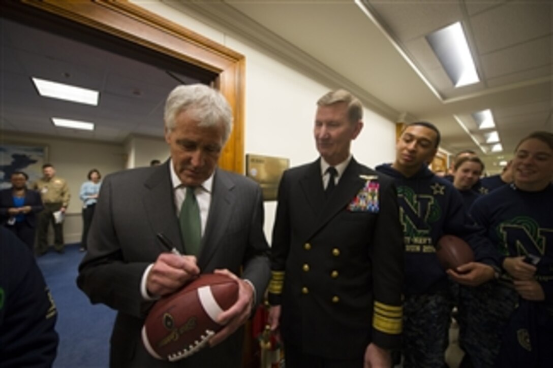 Defense Secretary Chuck Hagel autographs a game ball during a pep rally for the U.S. Naval Academy Midshipmen before the upcoming Army-Navy football game at the Pentagon, Dec. 11, 2014. 