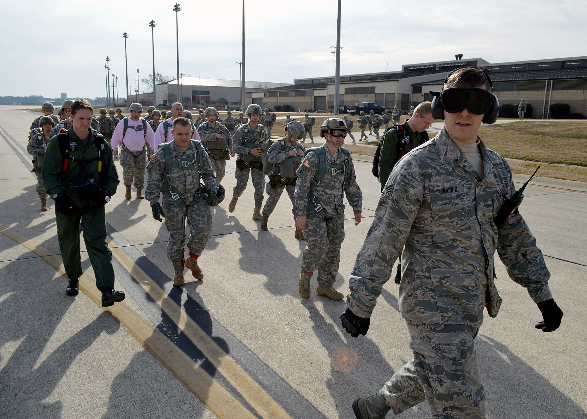 U.S. Air Force Senior Airman Steven Kaiser, a passenger services agent from the 3rd Aerial Port Squadron, escorts U.S. Army and foreign paratroopers on Green Ramp to a C-130 Hercules aircraft during the 17th Annual Randy Oler Memorial Operation Toy Drop on Dec. 5 at Green Ramp, Pope Army Airfield, Fort Bragg, North Carolina. Operation Toy Drop is the world’s largest combined airborne operation where Soldiers donate a toy to receive a lottery ticket number that are then randomly drawn for an opportunity to train and jump with foreign jumpmasters over Sicily Drop Zone. Foreign jumpmasters from Poland, Italy, Latvia, Germany, Indonesia and the Netherlands participated in this year’s event. Last year, Operation Toy Drop collected more than 12,000 toys that were donated to local charities and organizations across North Carolina. (U.S. Air Force photo/Marvin Krause)