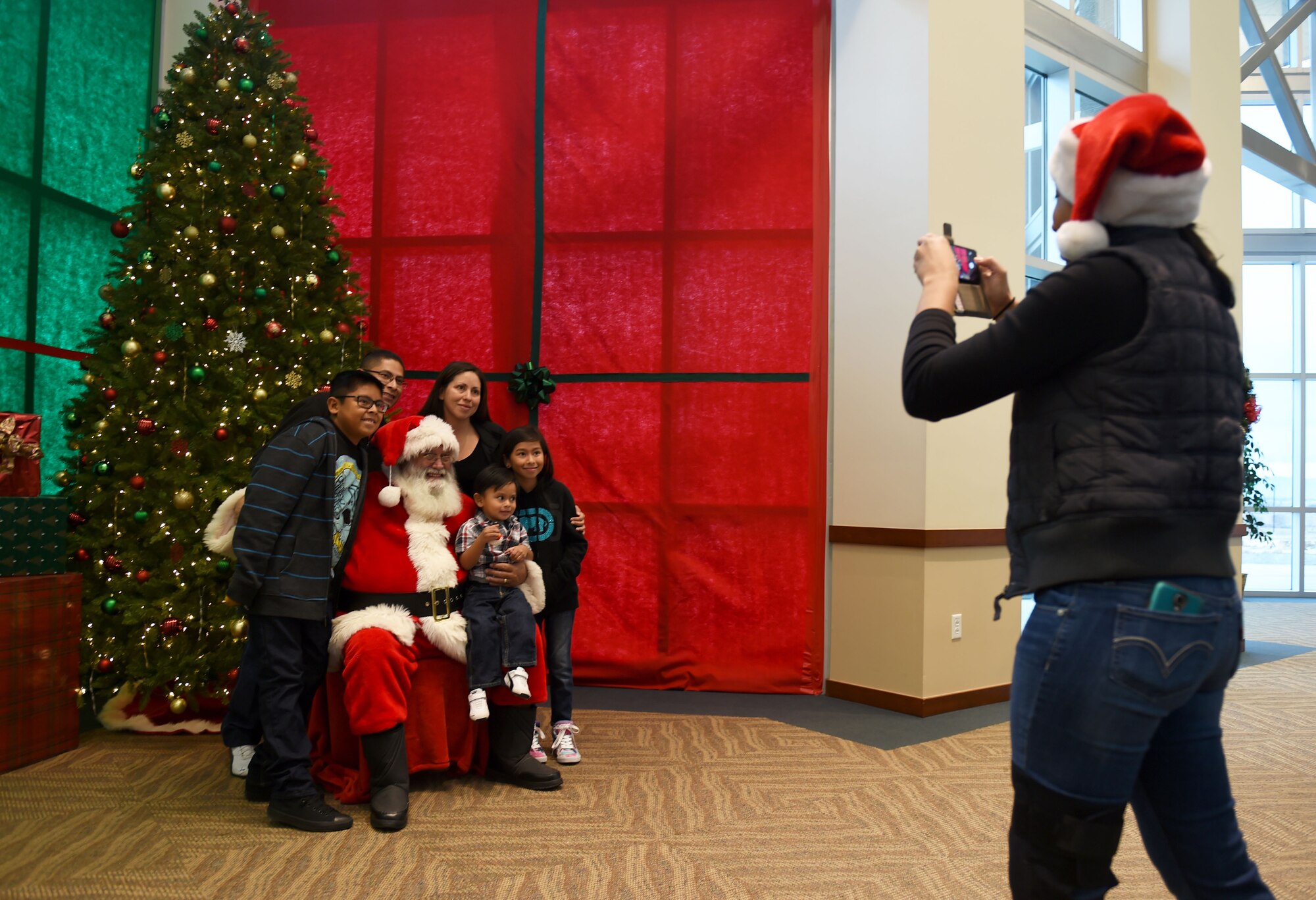 A volunteer takes a photo of a family while they sit with Santa Claus at the annual Breakfast with Santa event Dec. 14, 2014, at the Leadership Development Center on base. At the event, Team Buckley had the opportunity to meet Mr. and Mrs. Claus, grab a pancake breakfast and pick out their favorites from a variety of gifts to raise holiday spirit. (U.S. Air Force photo by Airman 1st Class Emily E. Amyotte/Released)