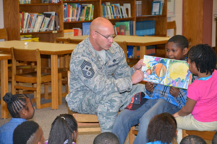 U.S. Air Force Chief Master Sgt. Scott Fuller, Ninth Air Force command chief, is assisted by Maurice and Ahnystie while reading to a group of first and second-grade students at Rafting Creek Elementary School, Rembert, S.C., Dec. 15, 2014. Fuller visits various public elementary schools throughout the year to help promote reading and strengthen community partnership. (U.S. Air Force photo by Master Sgt. Latisha Cole/Released)