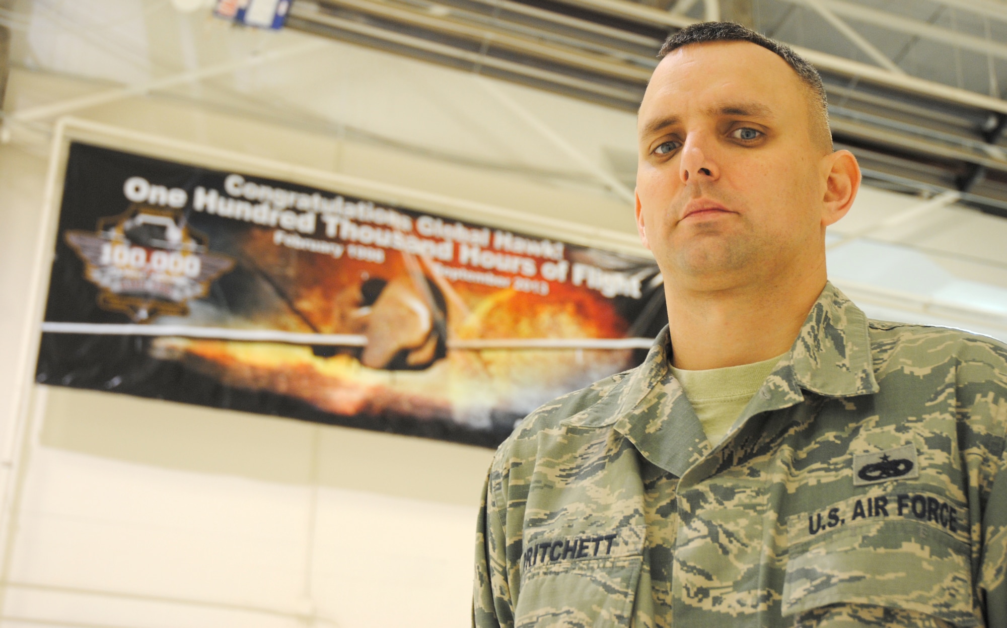 Cutline: Tech. Sgt. Darrell Pritchett, 69th Maintenance Squadron specialist expediter, poses for a photo Dec. 10, 2014, in front of the 100,000 flying hours commemorative banner located inside a hangar on Grand Forks Air Force Base, N.D. As a member of the 69th MXS, Pritchett helped maintain Global Hawks that helped reach that milestone. (U.S. Air Force photo/Staff Sgt. Luis Loza Gutierrez)
