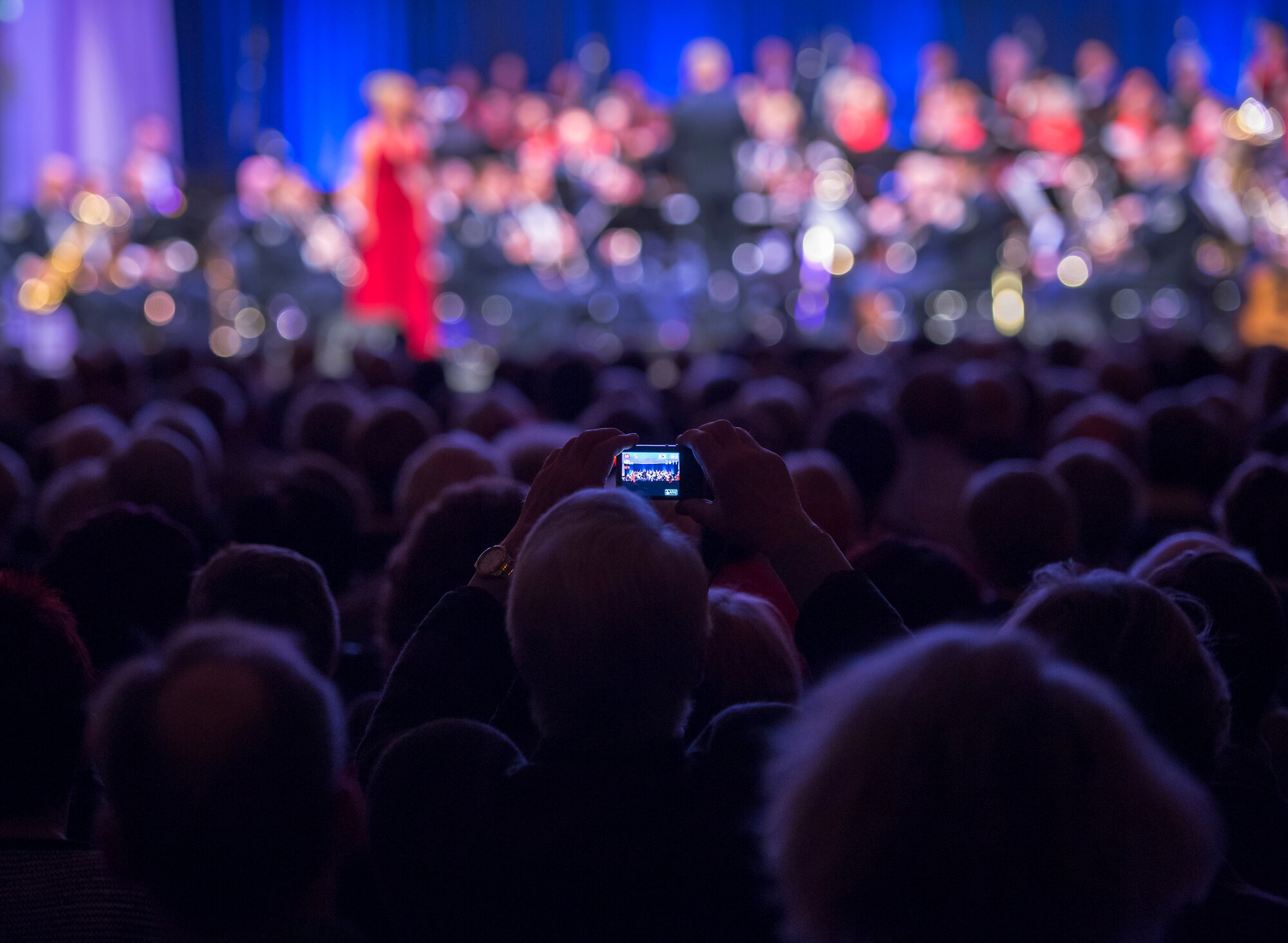An audience member takes a photo of the U. S. Air Forces in Europe Band and the Rheinland-Pfalz International Choir as they perform during the annual KMC Christmas Concert, Kaiserslautern, Germany, Dec. 12, 2014. The band and choir performed and sang a wide variety of holiday songs in English and German. (U.S. Air Force photo/Senior Airman Damon Kasberg)