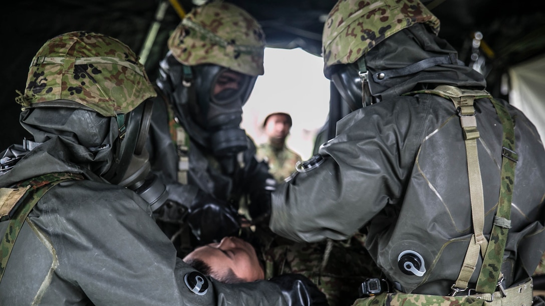 Japan Ground Self-Defense Force members with the Special Weapons Protection Unit remove clothing from a casualty during an exercise Dec. 1 at Camp Naha, Okinawa. The casualty went through an immediate evacuation from the area prior to being treated. Participating U.S. Marine chemical, biological, radiological and nuclear defense specialists then wrapped the casualty in a blanket and went through the full decontamination process. The JGSDF personnel are with the Nuclear Biological Chemical Unit, 15th Brigade. 